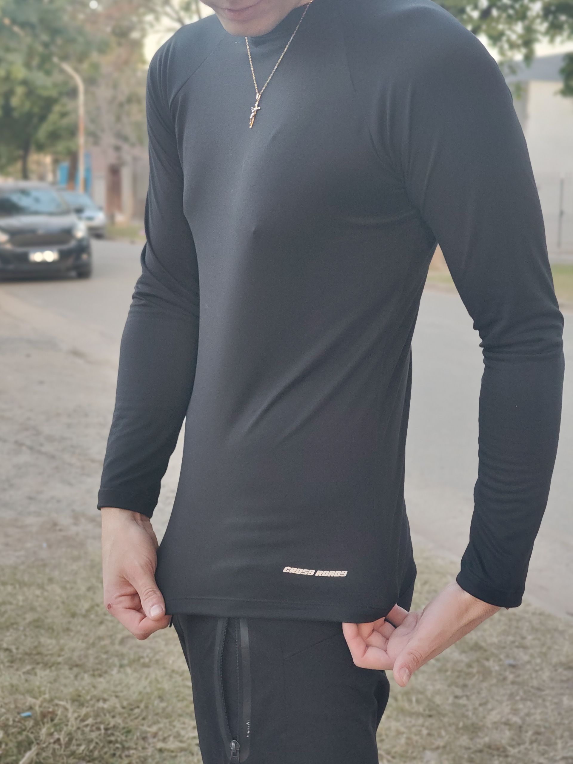 Hombre con camisa negra de manga larga, de pie afuera, sosteniendo el dobladillo de la camisa.