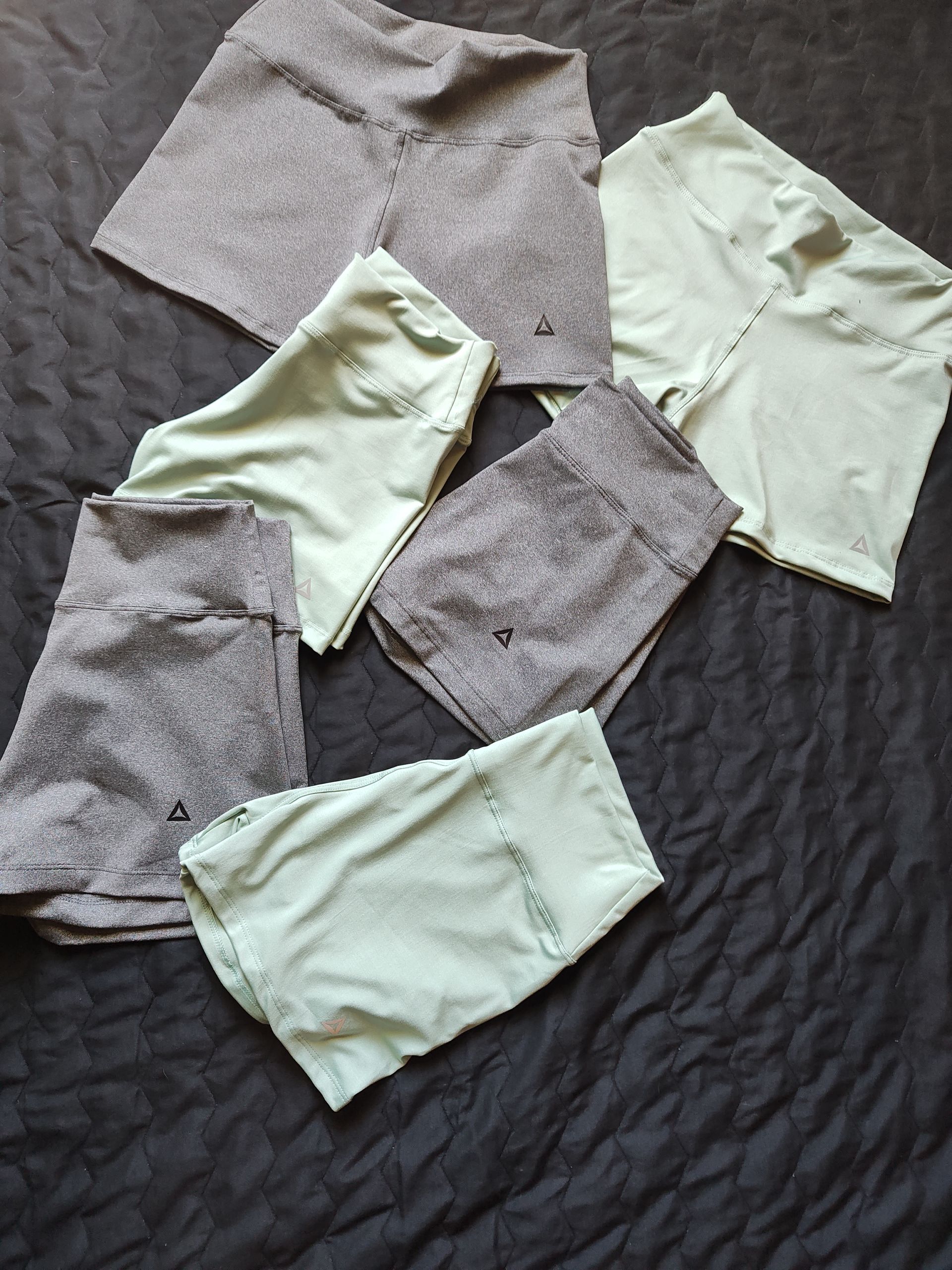 Mujer con pantalones cortos grises y zapatillas de deporte parada en una calle, ajustándose la camisa.