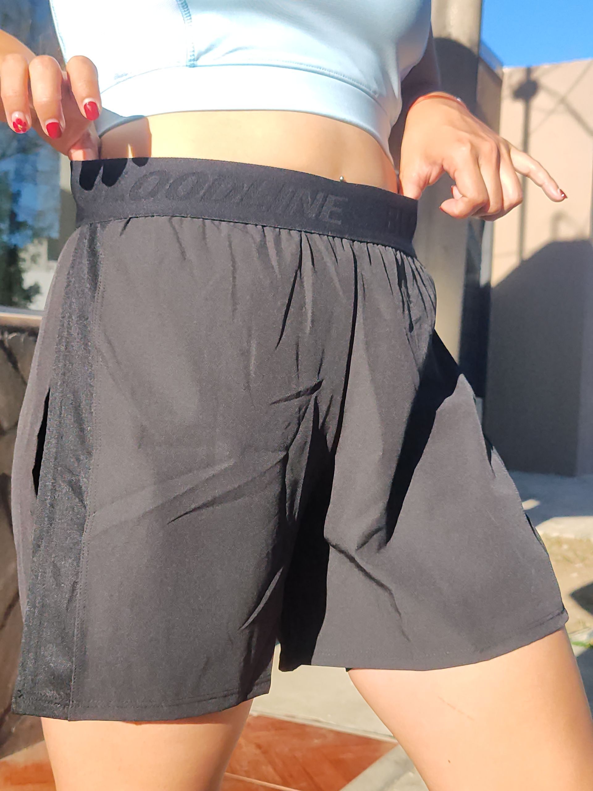 Mujer en pantalones cortos deportivos negros, top azul claro, al aire libre, tocando pantalones cortos.