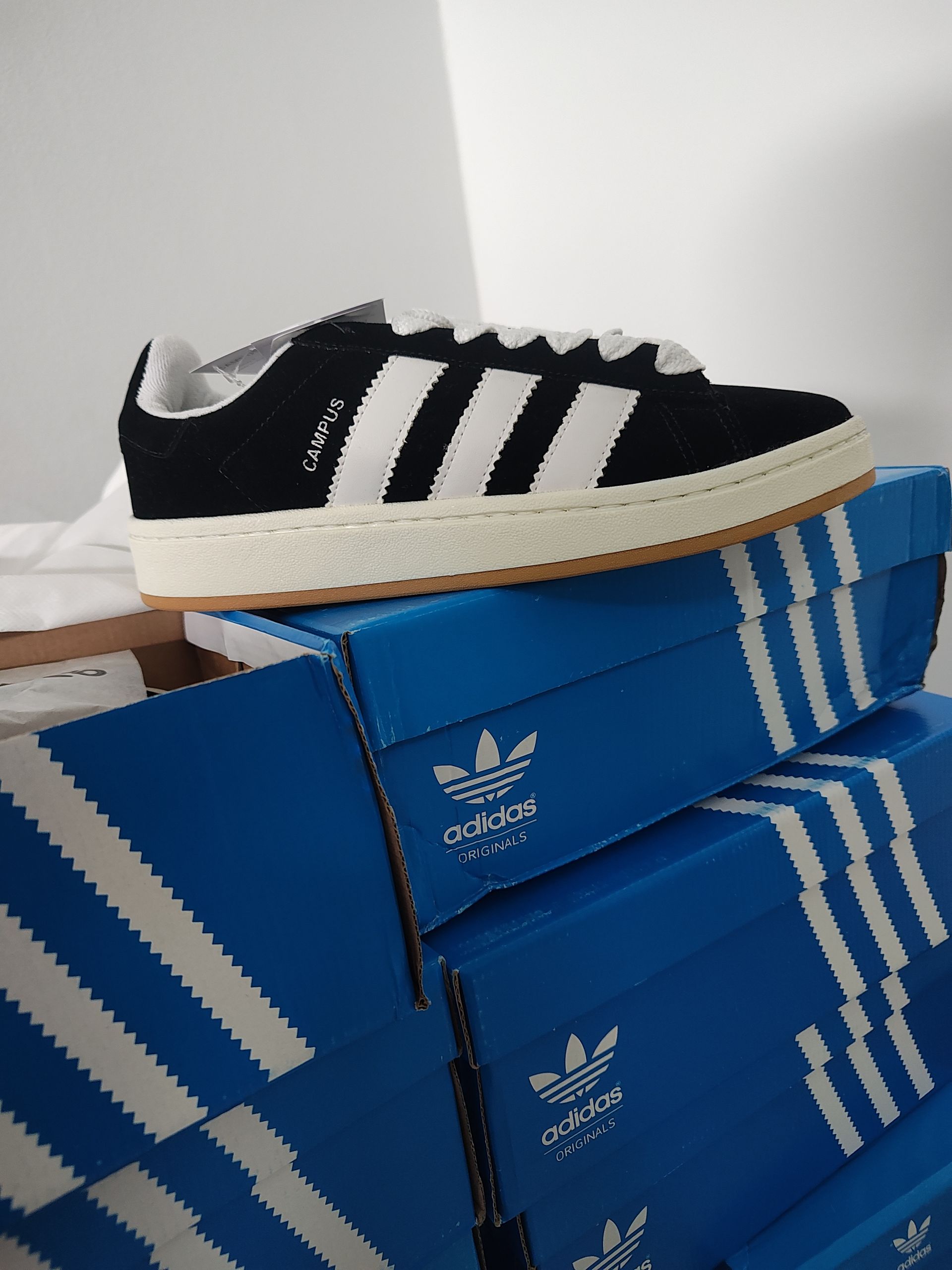 Zapatilla Adidas en blanco y negro sobre una caja de rayas azules y blancas, sobre un fondo de estantes.