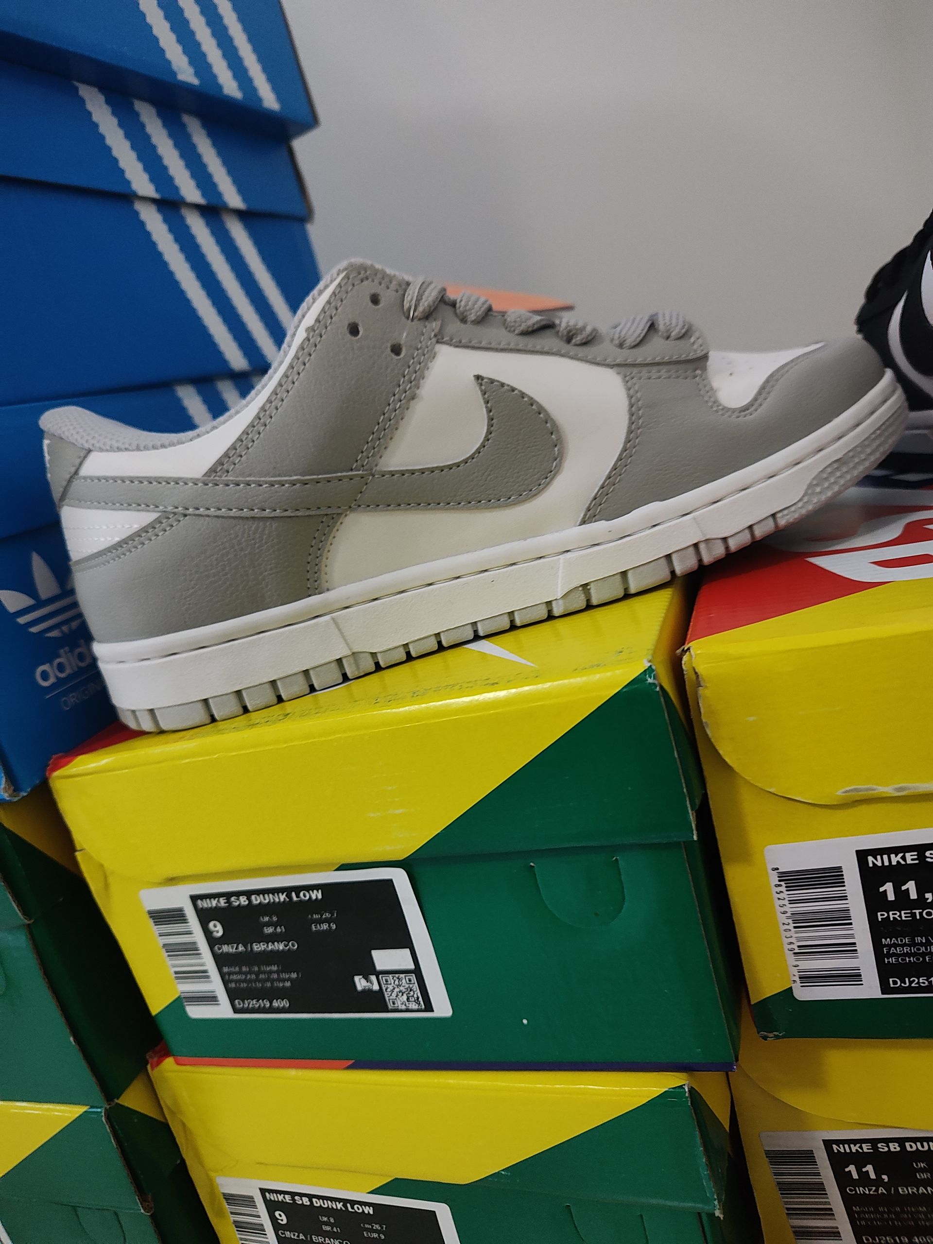 Zapatilla Nike Dunk Low gris y blanca en una caja colorida, con un estante de madera al fondo.