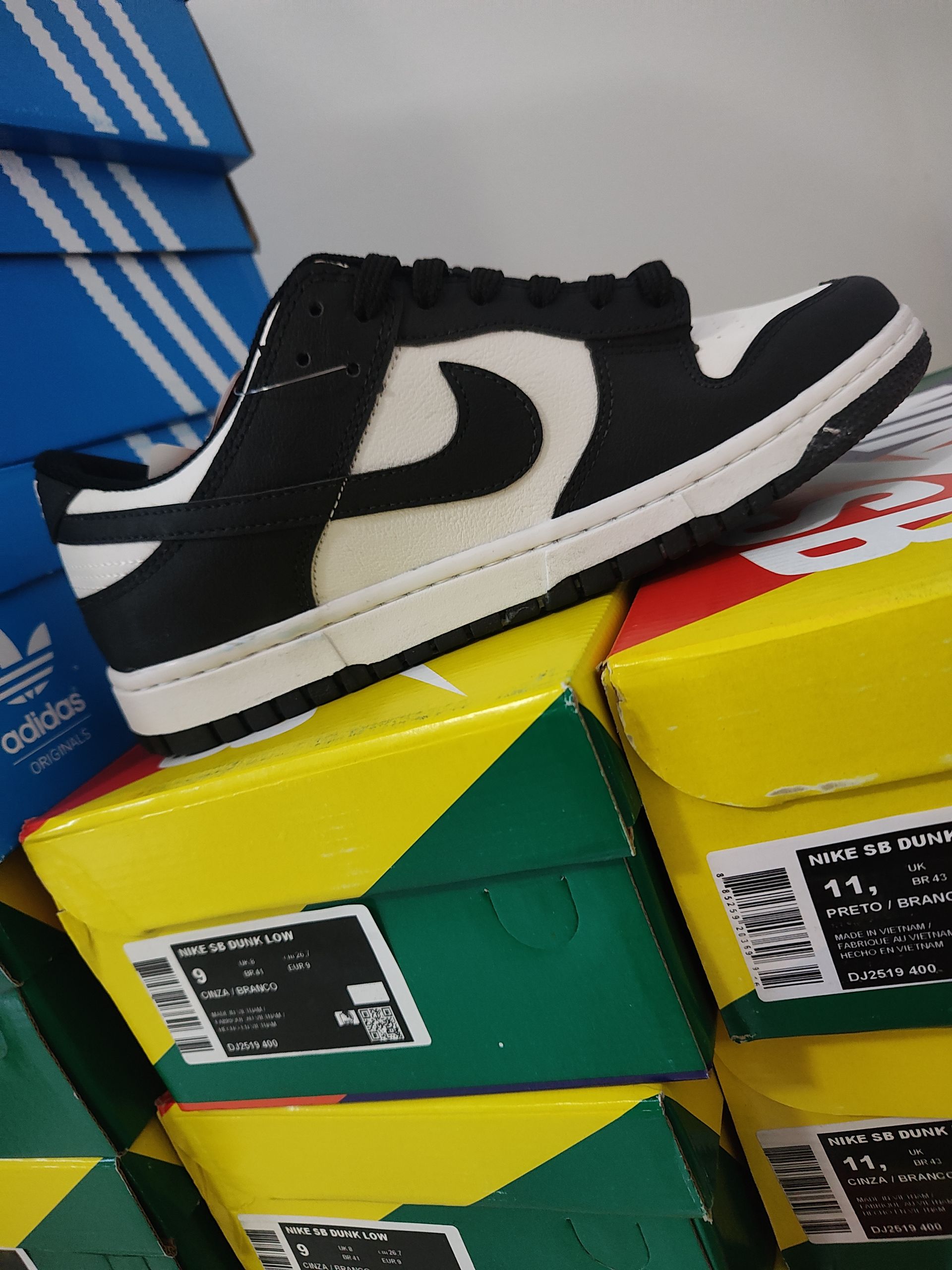 Zapatilla Nike Dunk Low en blanco y negro en una caja colorida, con un estante de madera en el fondo.