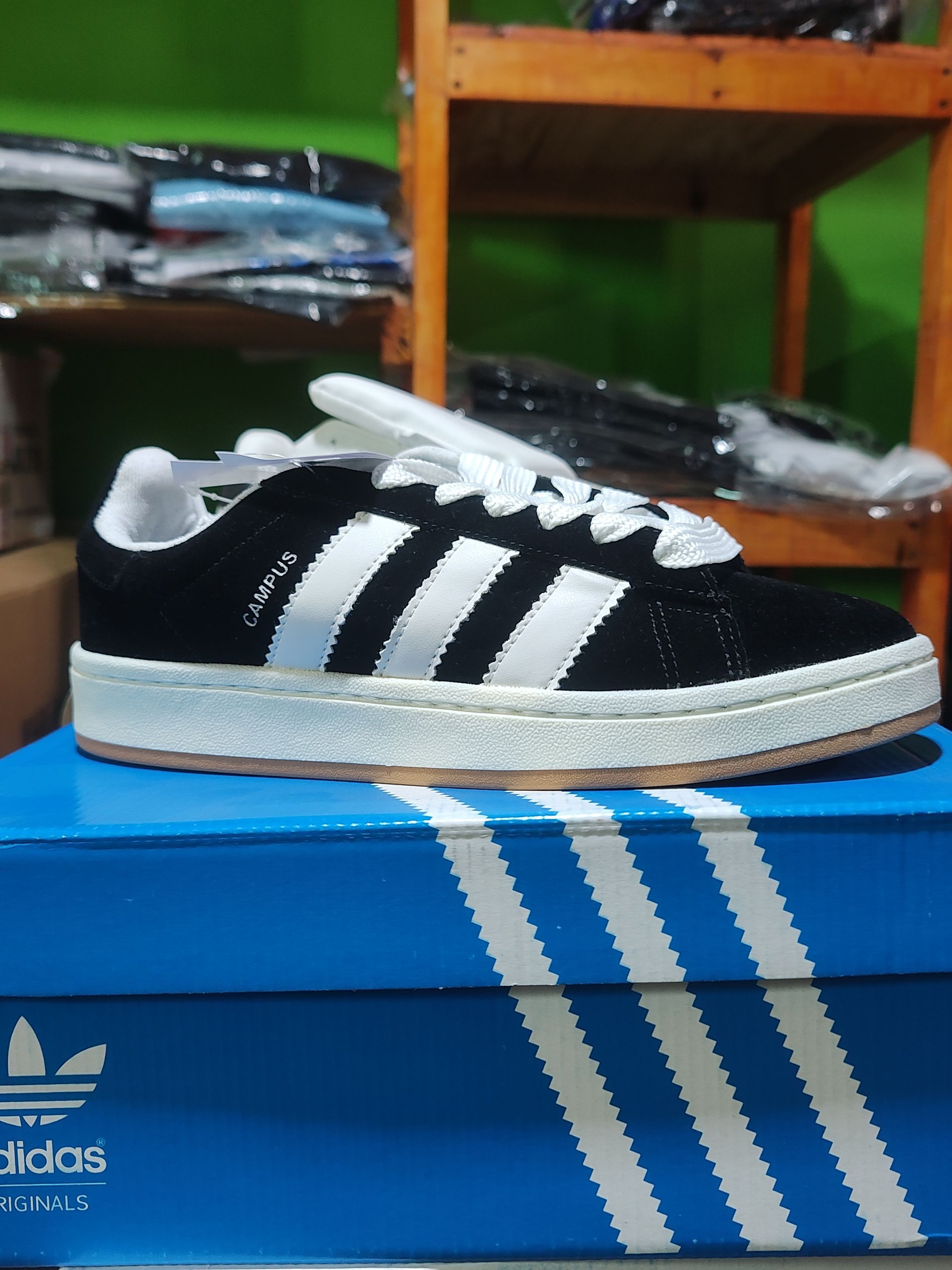 Zapatilla Adidas en blanco y negro sobre una caja de rayas azules y blancas, sobre un fondo de estantes.