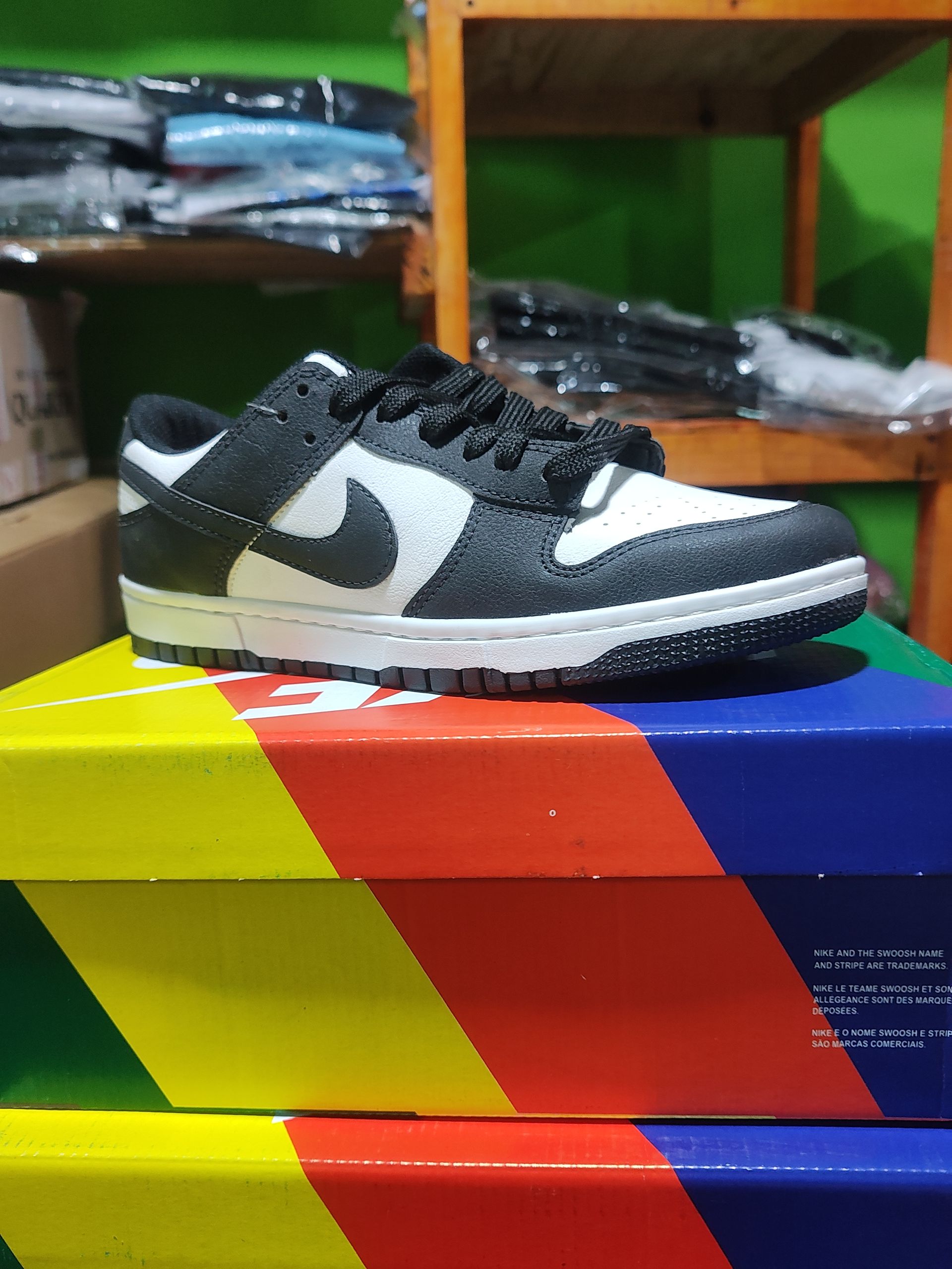 Zapatilla Nike Dunk Low en blanco y negro en una caja colorida, con un estante de madera en el fondo.
