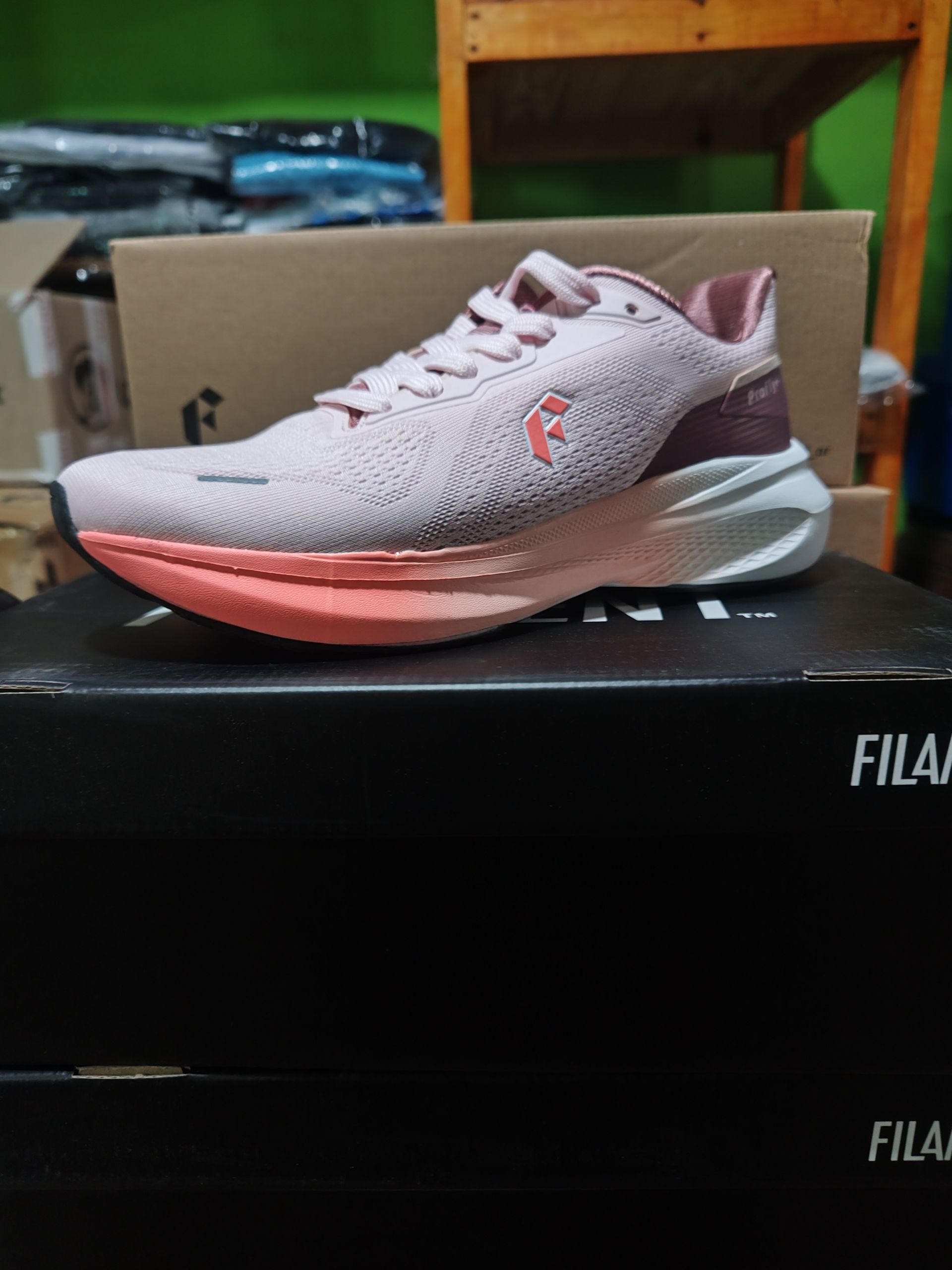 Zapatilla de running rosa y burdeos con suela coral, encima de una caja FILA negra.