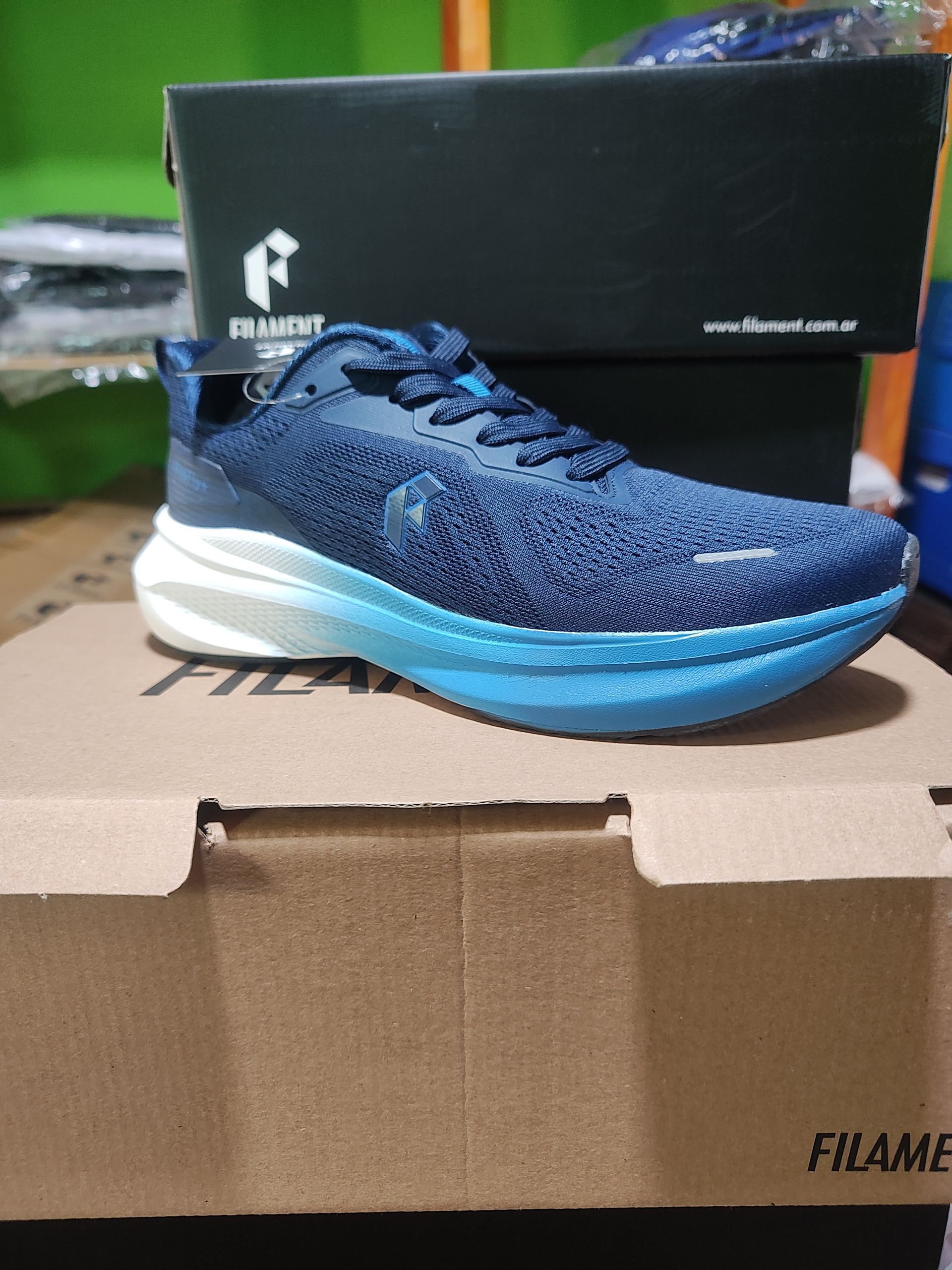 Zapatilla de running de color azul sobre una caja de cartón, con una caja de zapatos al fondo.