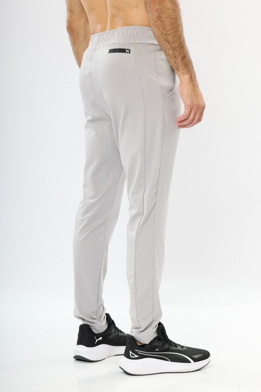 Un hombre sin camisa lleva un par de pantalones deportivos grises y zapatos negros.