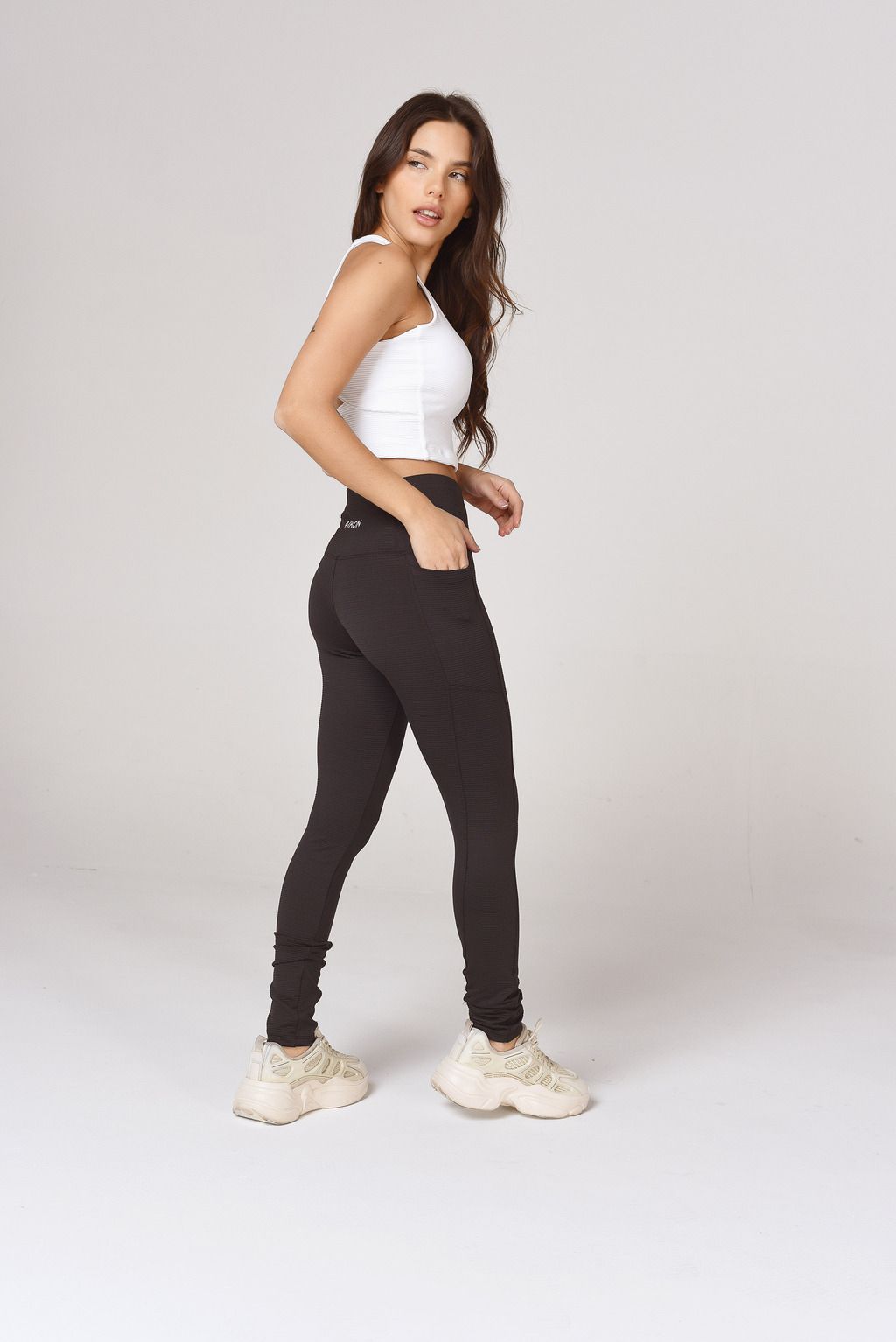 La mujer lleva una camiseta blanca sin mangas y leggings negros.