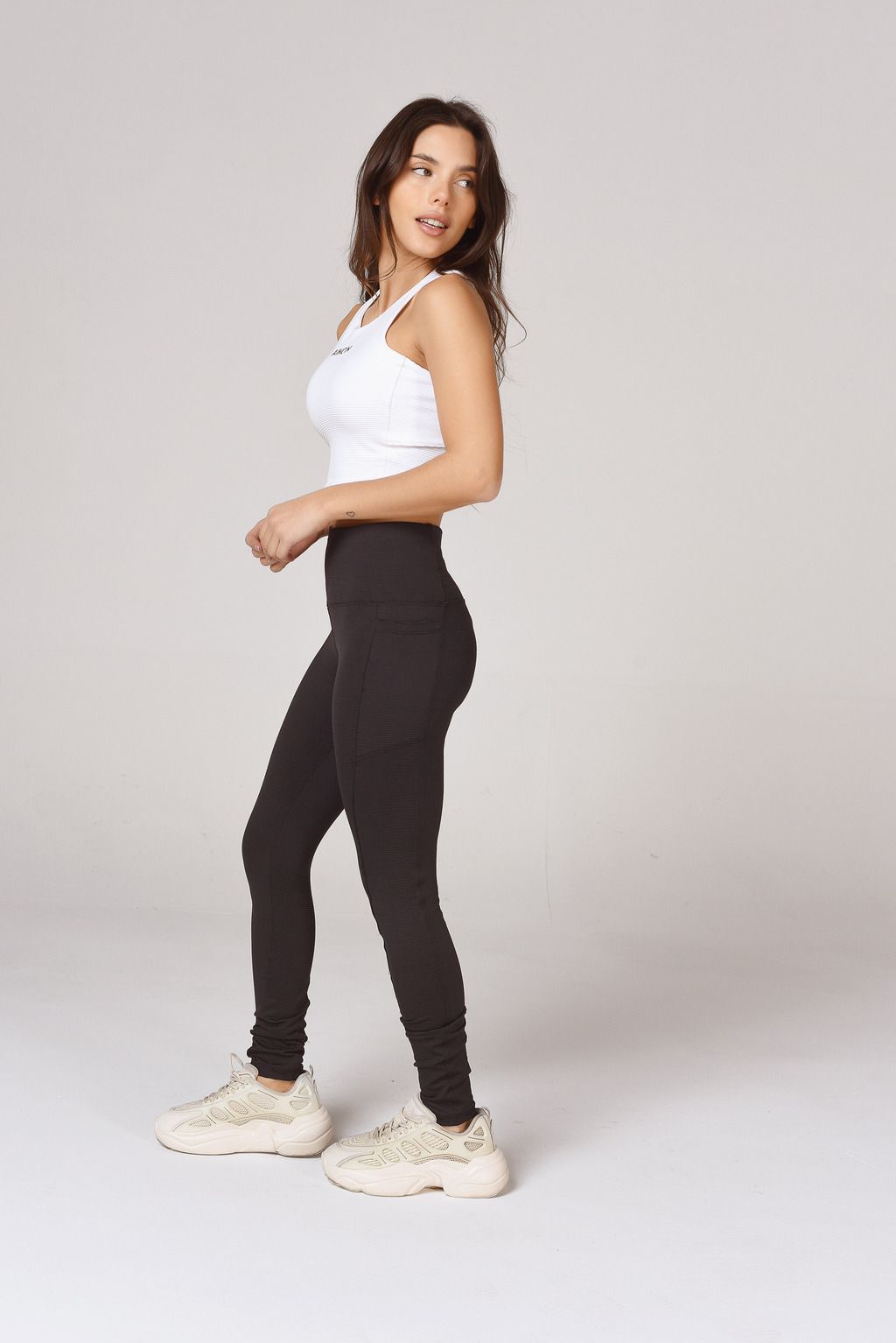 La mujer lleva una camiseta blanca sin mangas y leggings negros.