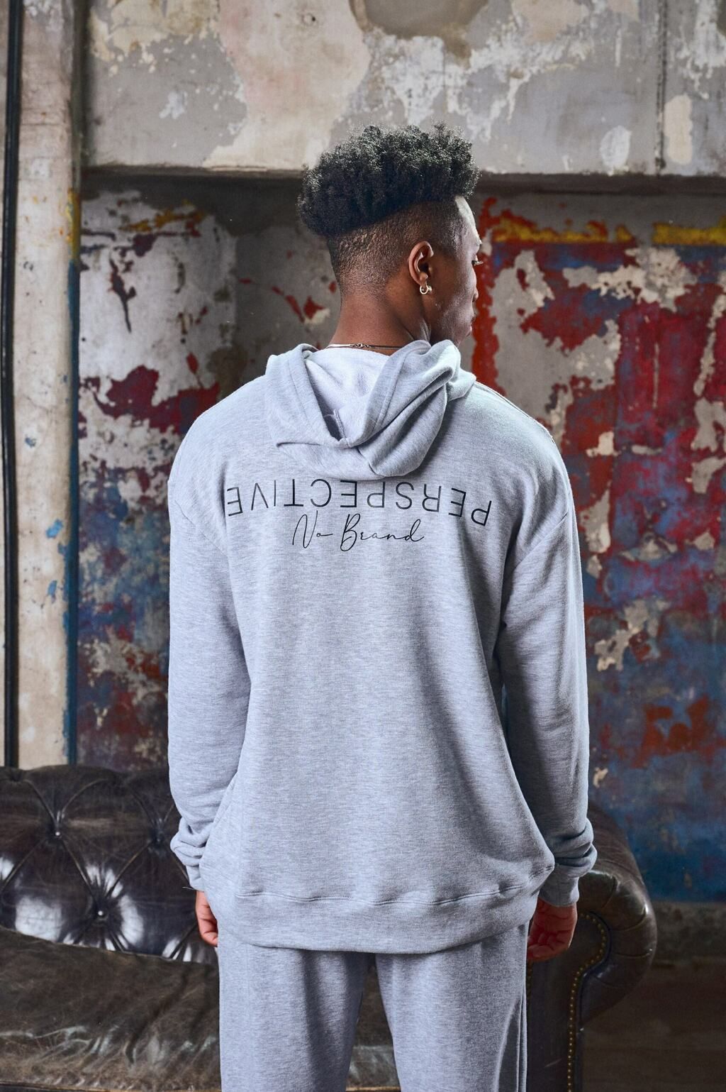 Un hombre con una sudadera con capucha gris y pantalones deportivos está de pie en un sofá.