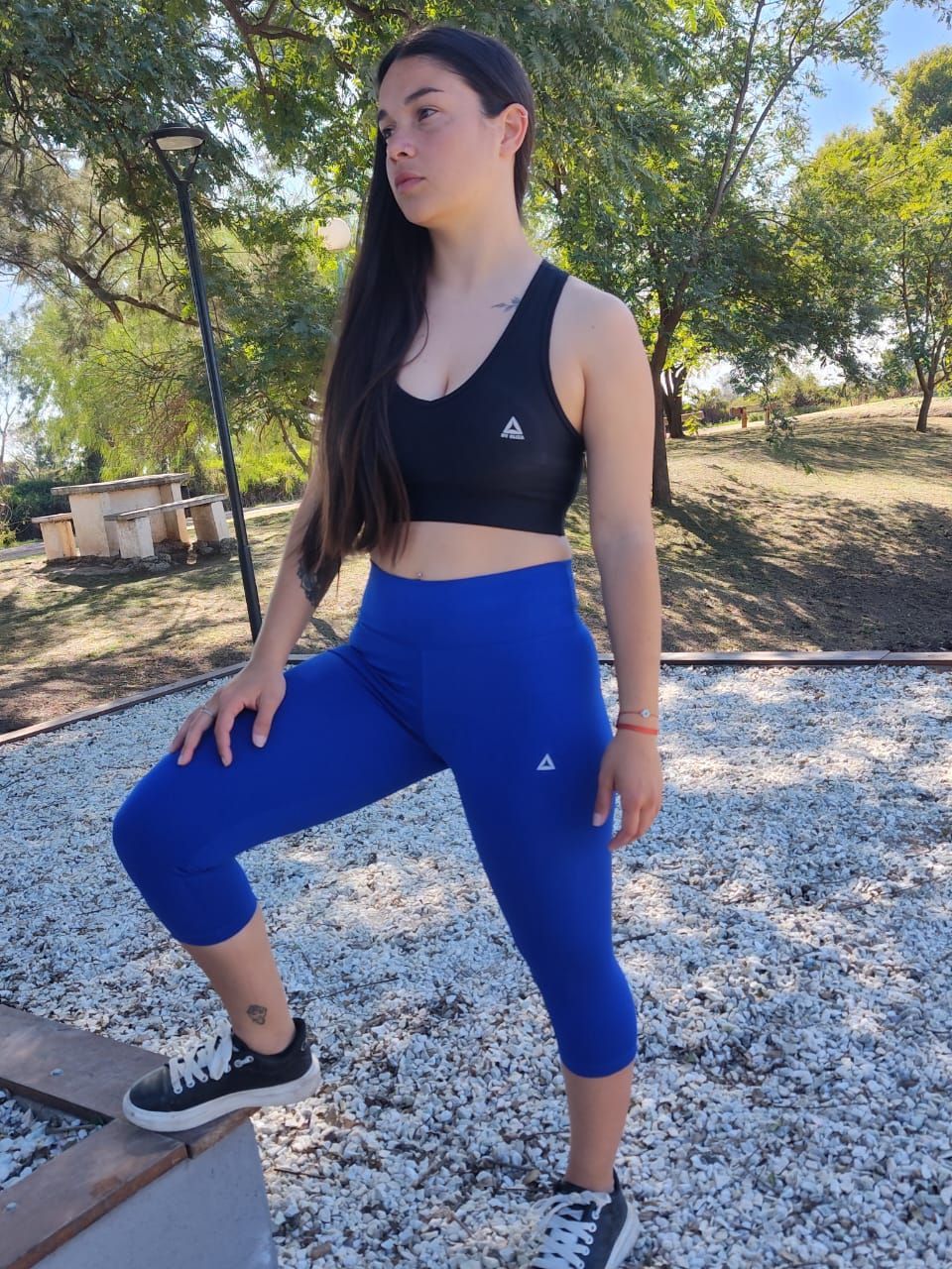 Una mujer con leggings azules y un sujetador deportivo negro posa al aire libre sobre una superficie de piedra.