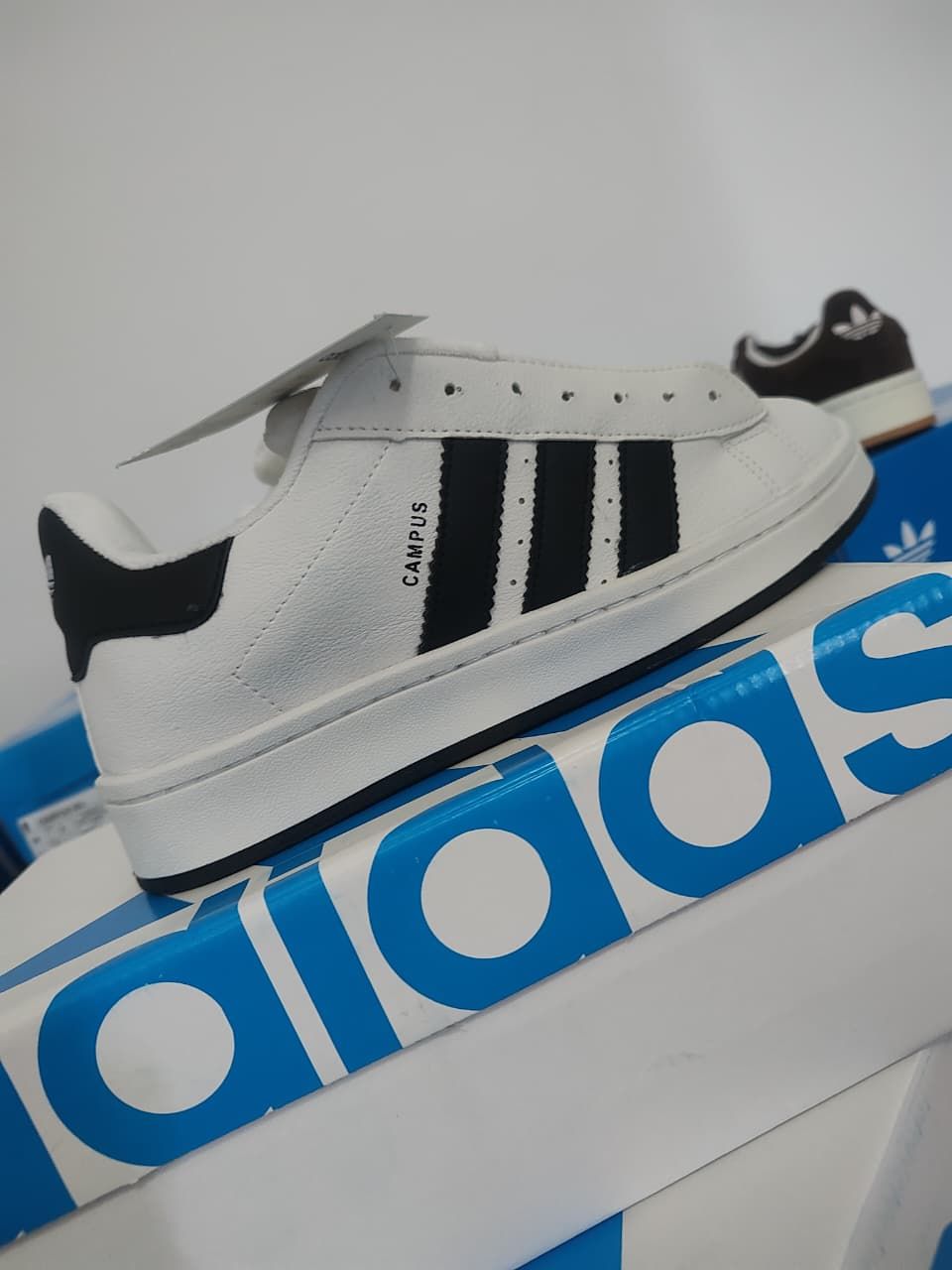 Zapato Campus de color blanco con rayas negras en una caja etiquetada 
