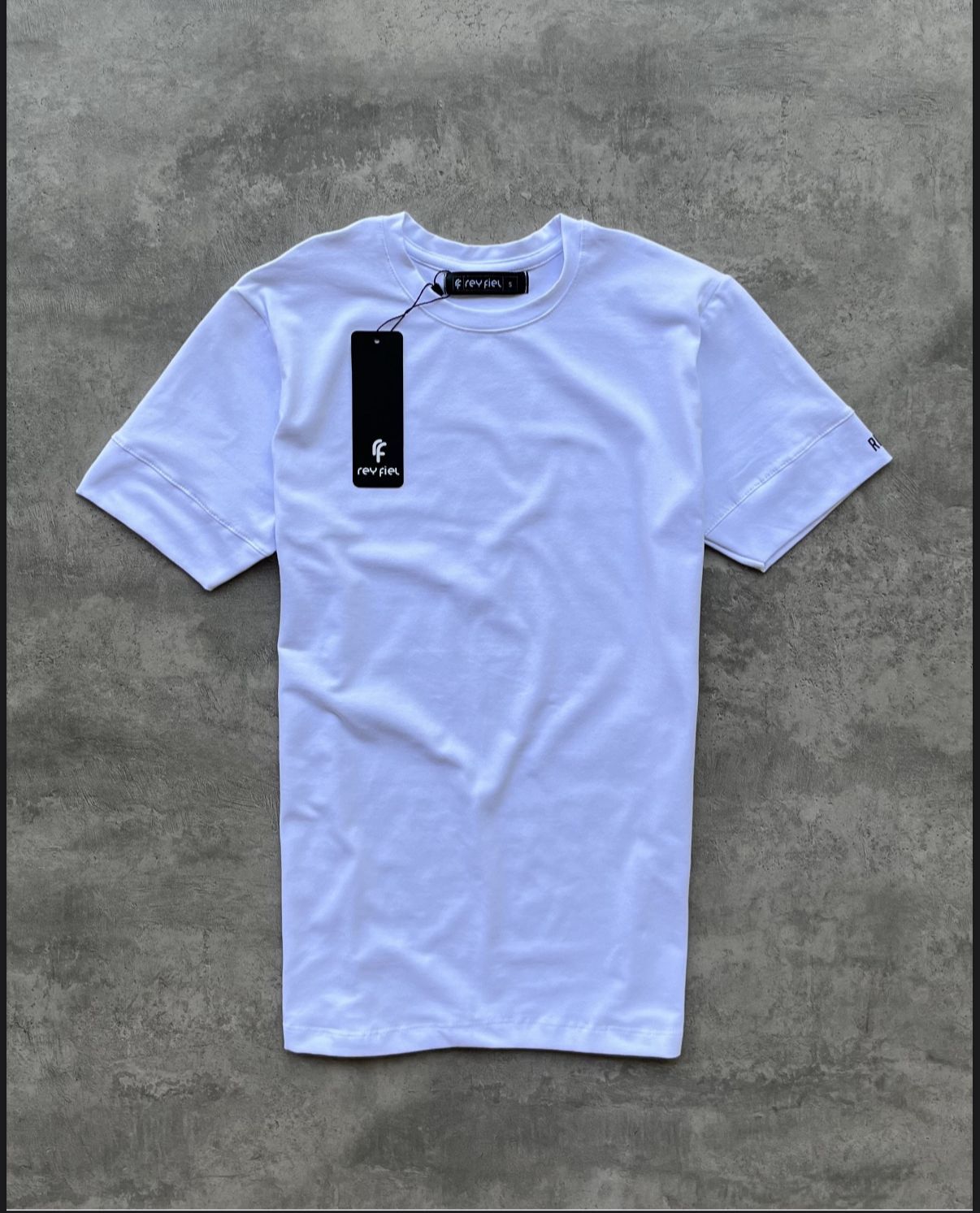 Camiseta negra con cuello redondo y etiqueta, colocada sobre una superficie gris.