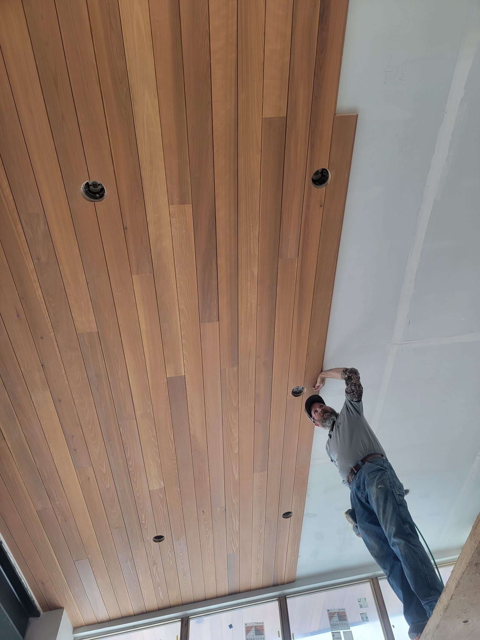 A man is working on a wooden ceiling in a room.