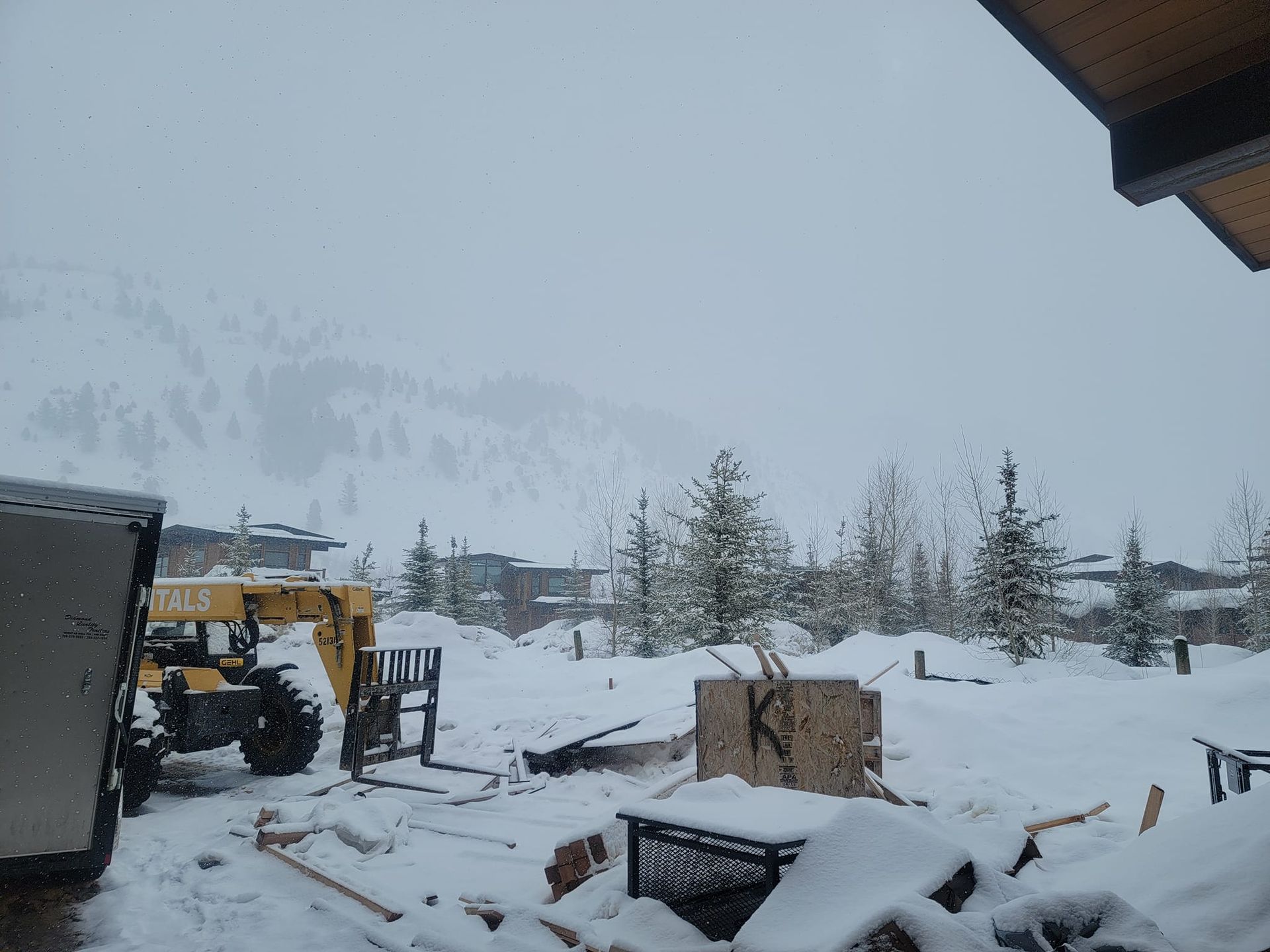 A yellow forklift is parked in the snow in front of a mountain.
