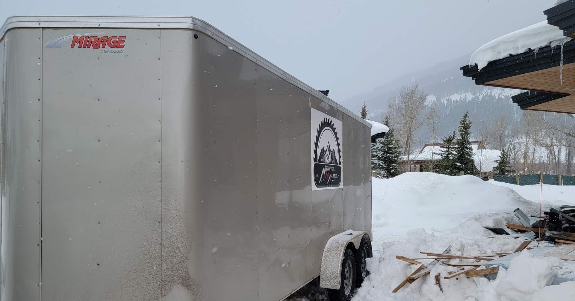A white trailer is parked in the snow in front of a house.