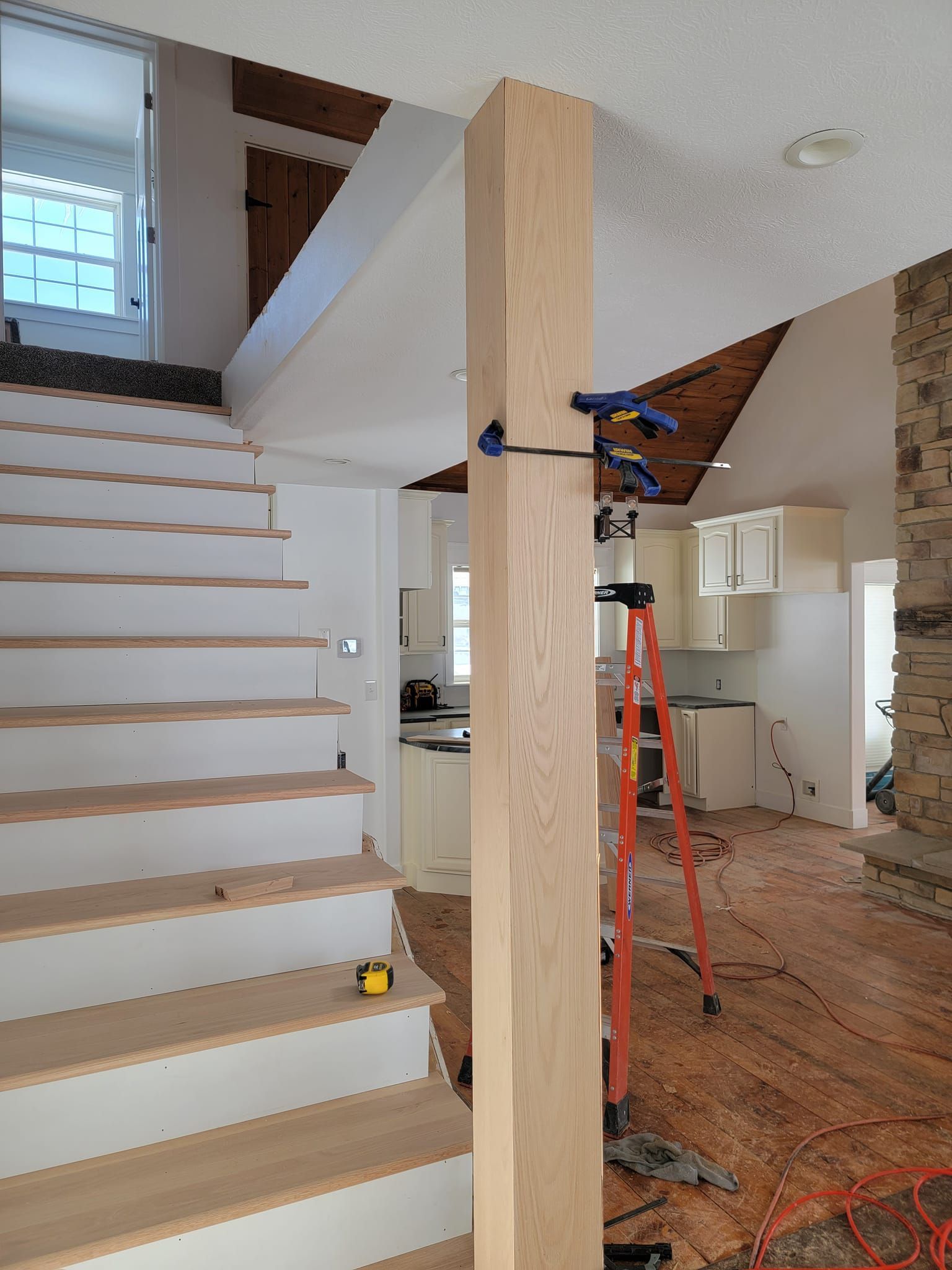 A ladder is sitting next to a wooden post in a room with stairs.