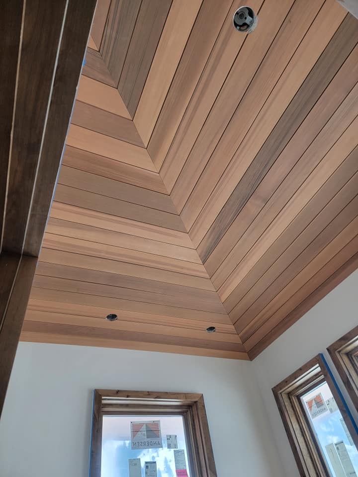 A room with a wooden ceiling and two windows.