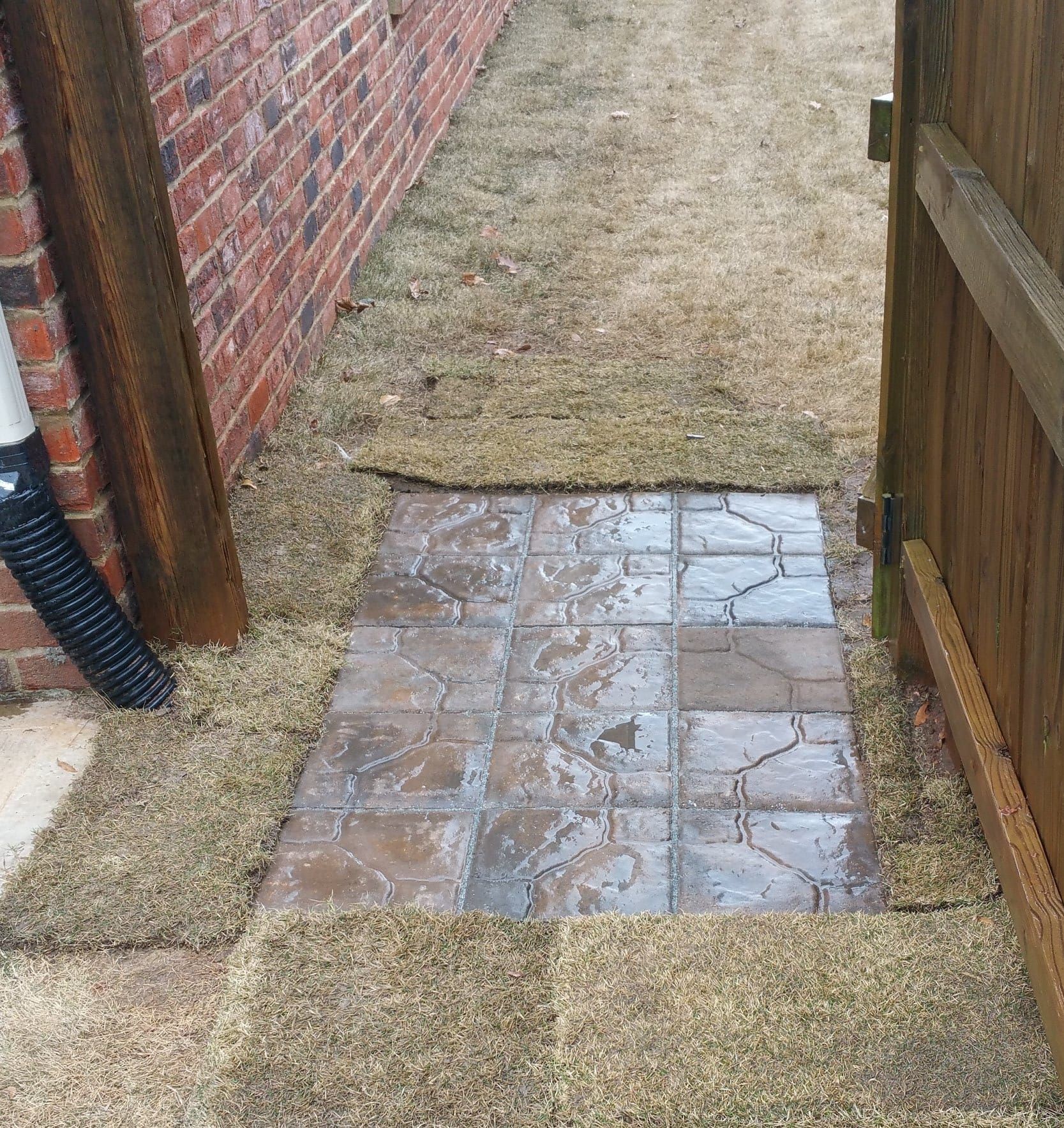 A brick walkway leading to a wooden fence next to a brick wall.
