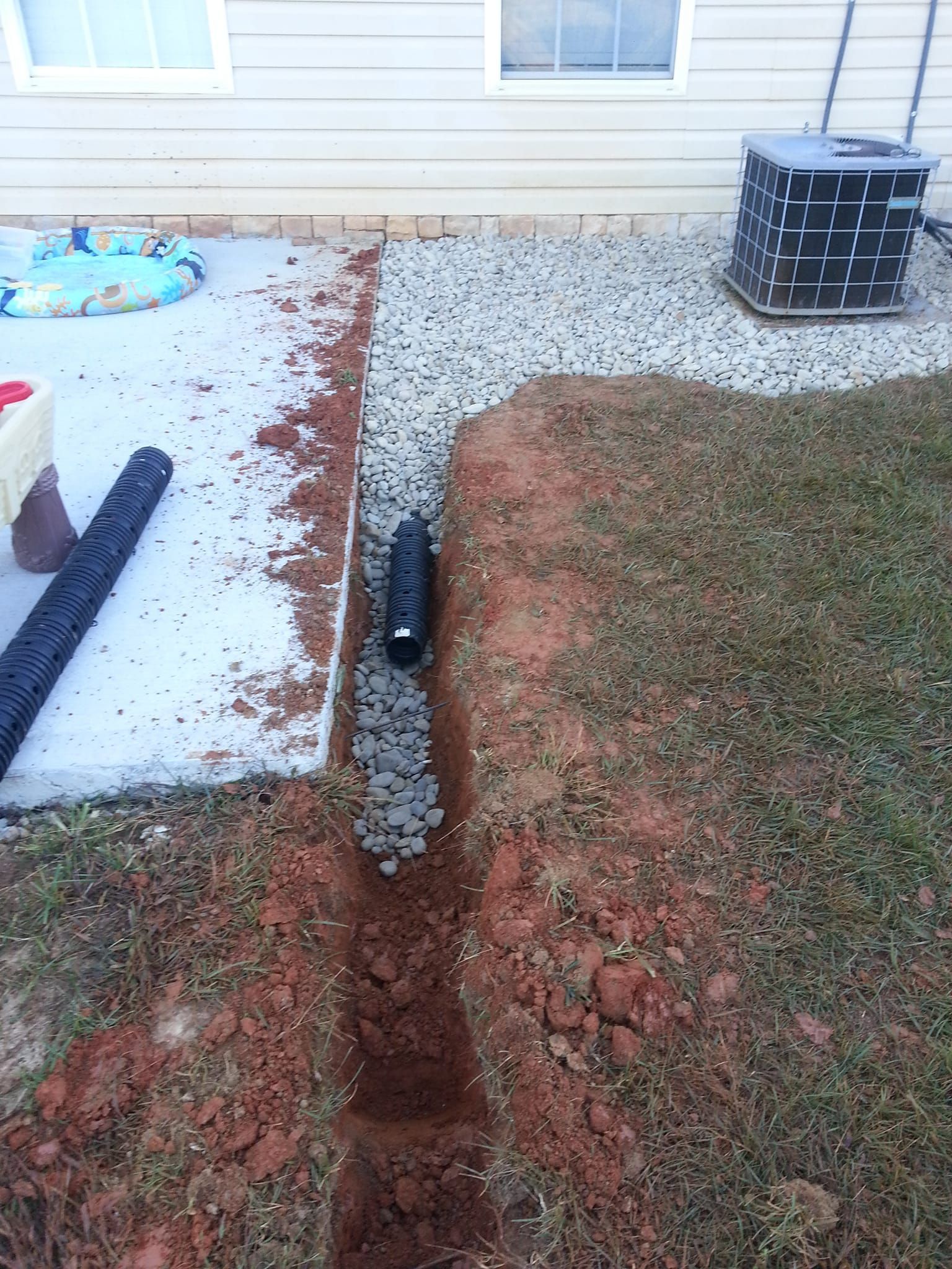A drain pipe is being installed in the dirt next to a house.