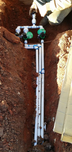 A person is working on a pipe in the dirt.