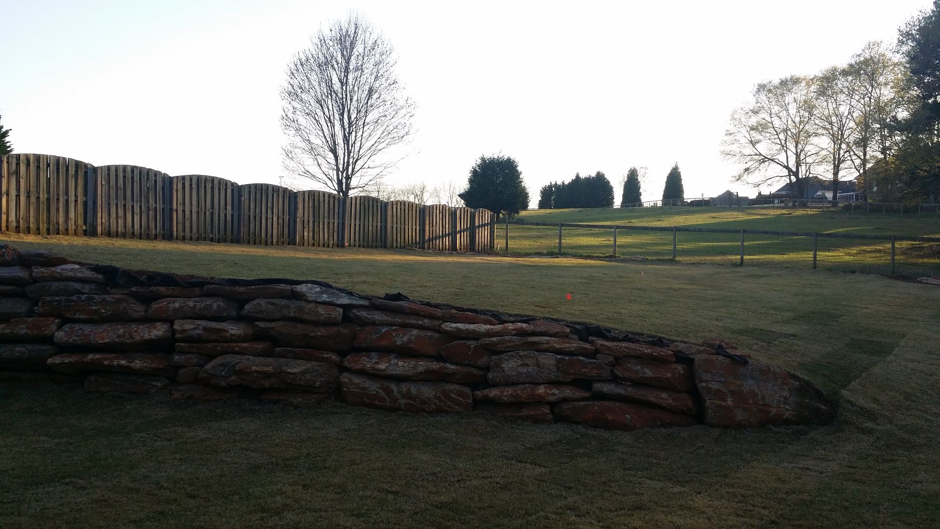 A wooden fence surrounds a grassy field with trees in the background southern shops
