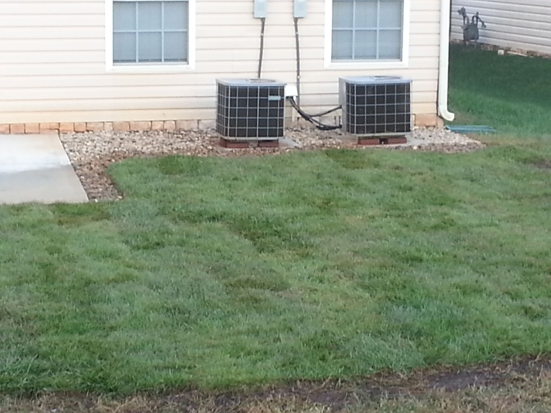 Two air conditioners are sitting in the grass in front of a house boiling springs