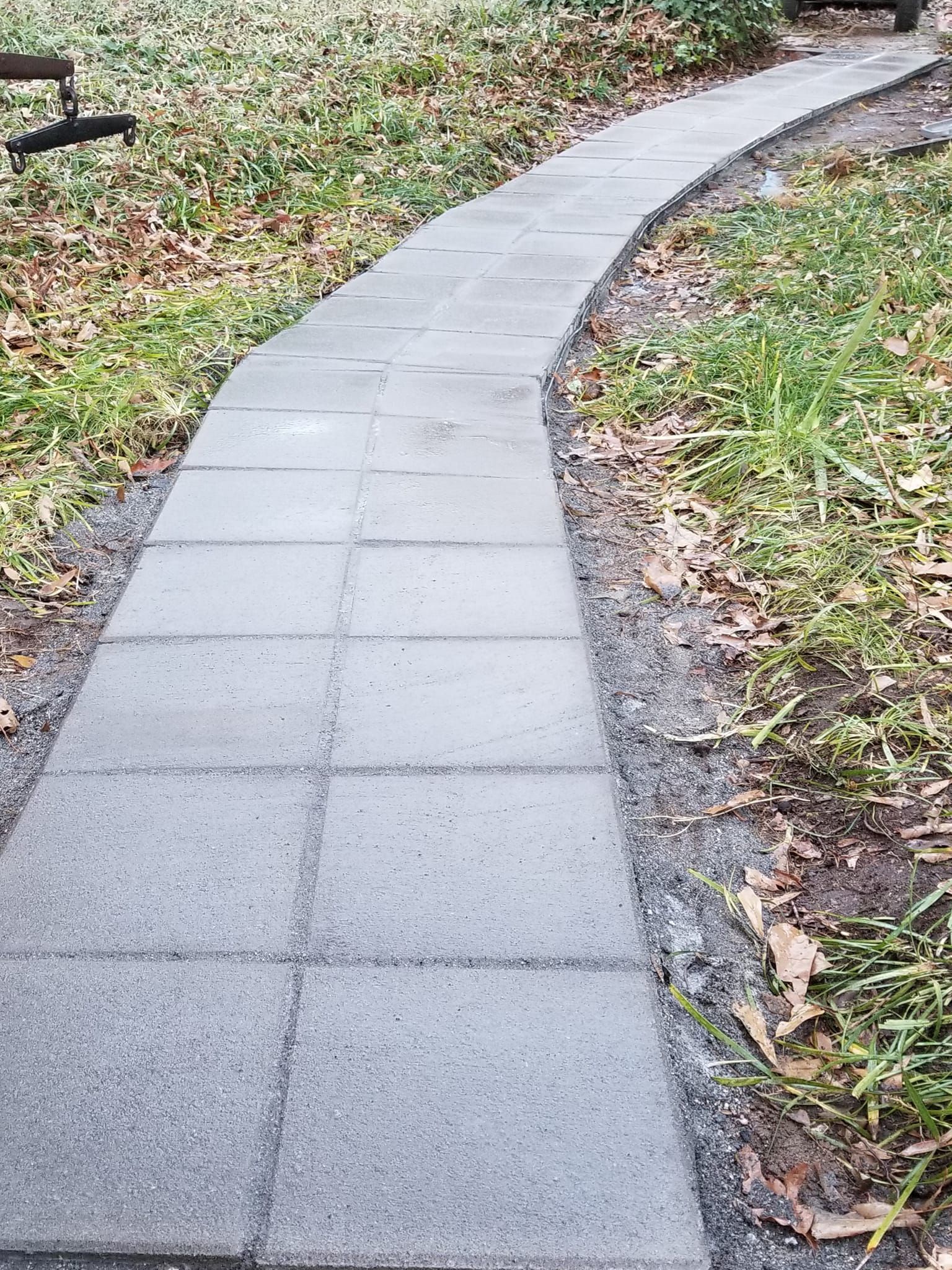 A brick walkway leading to a bench in a park.
