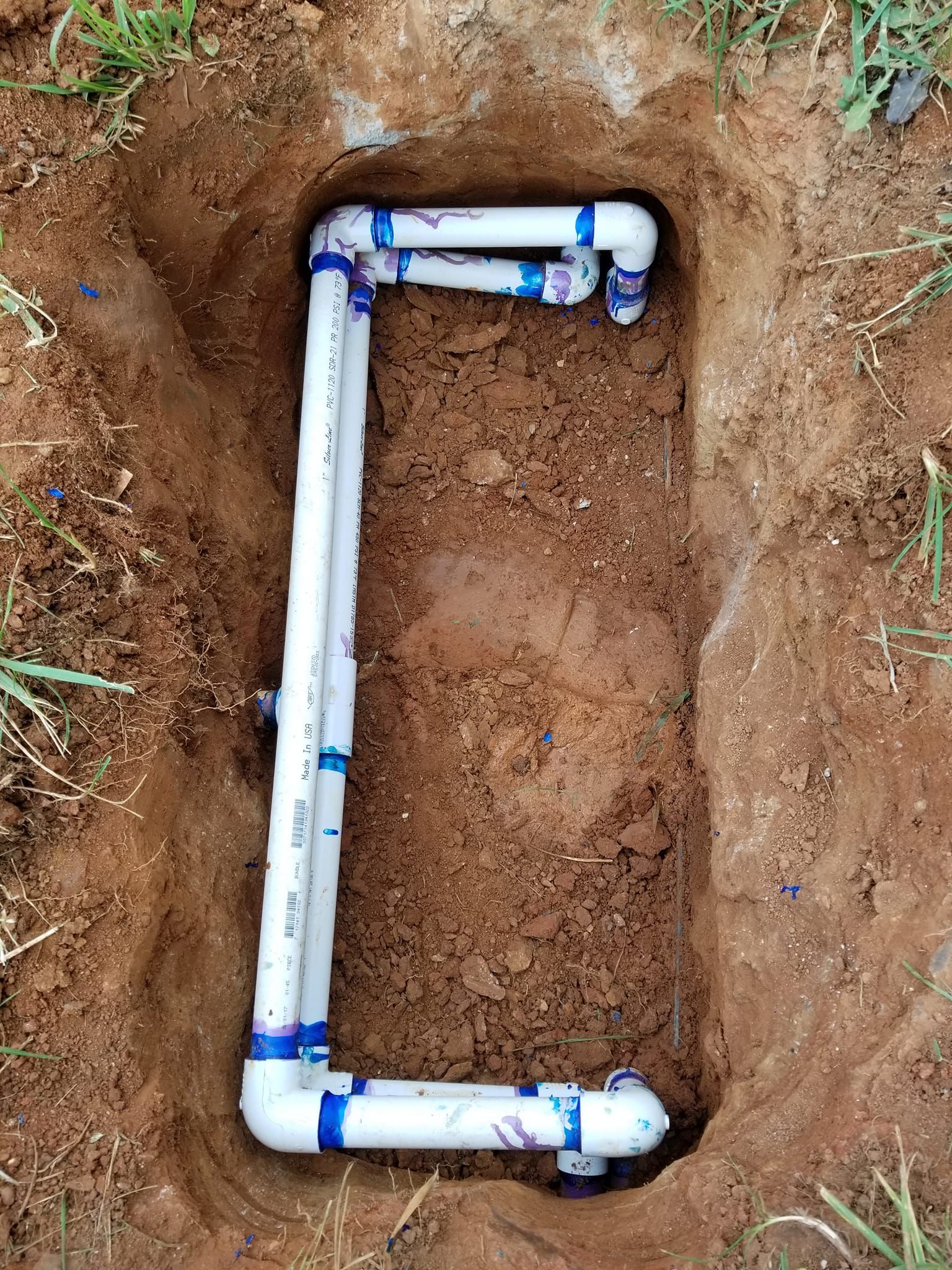A white pipe is laying in the dirt in a hole.