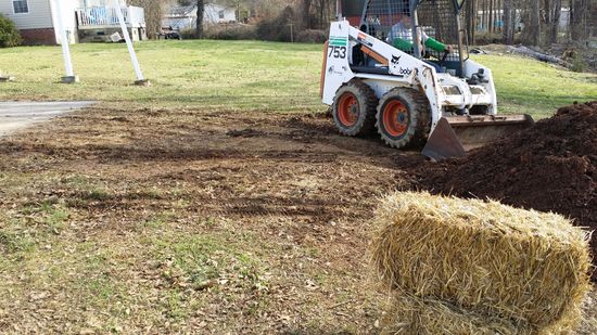 A bulldozer is moving dirt in a yard next to a bale of hay.