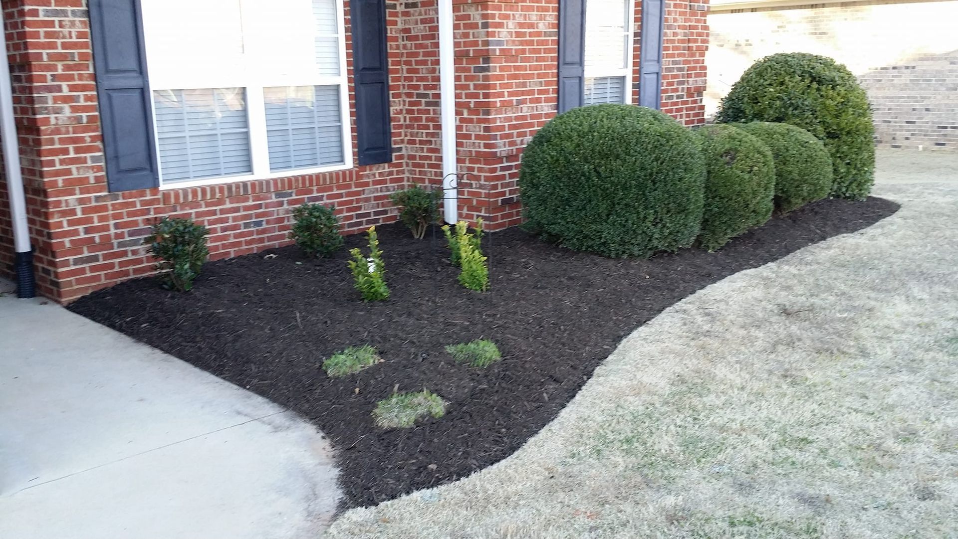 A brick house with a lush green lawn and bushes in front of it. duncan 