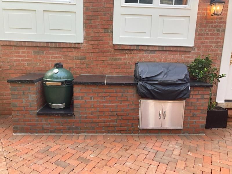 A grill is sitting on a brick wall next to a green egg.