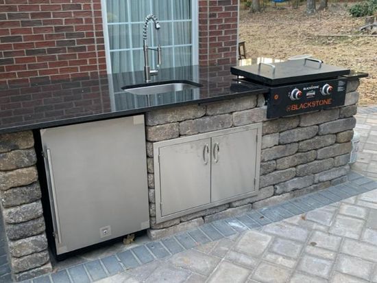 An outdoor kitchen with a sink , grill , and dishwasher.