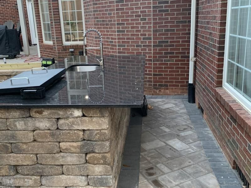 A kitchen island with a sink and a grill in front of a brick building.