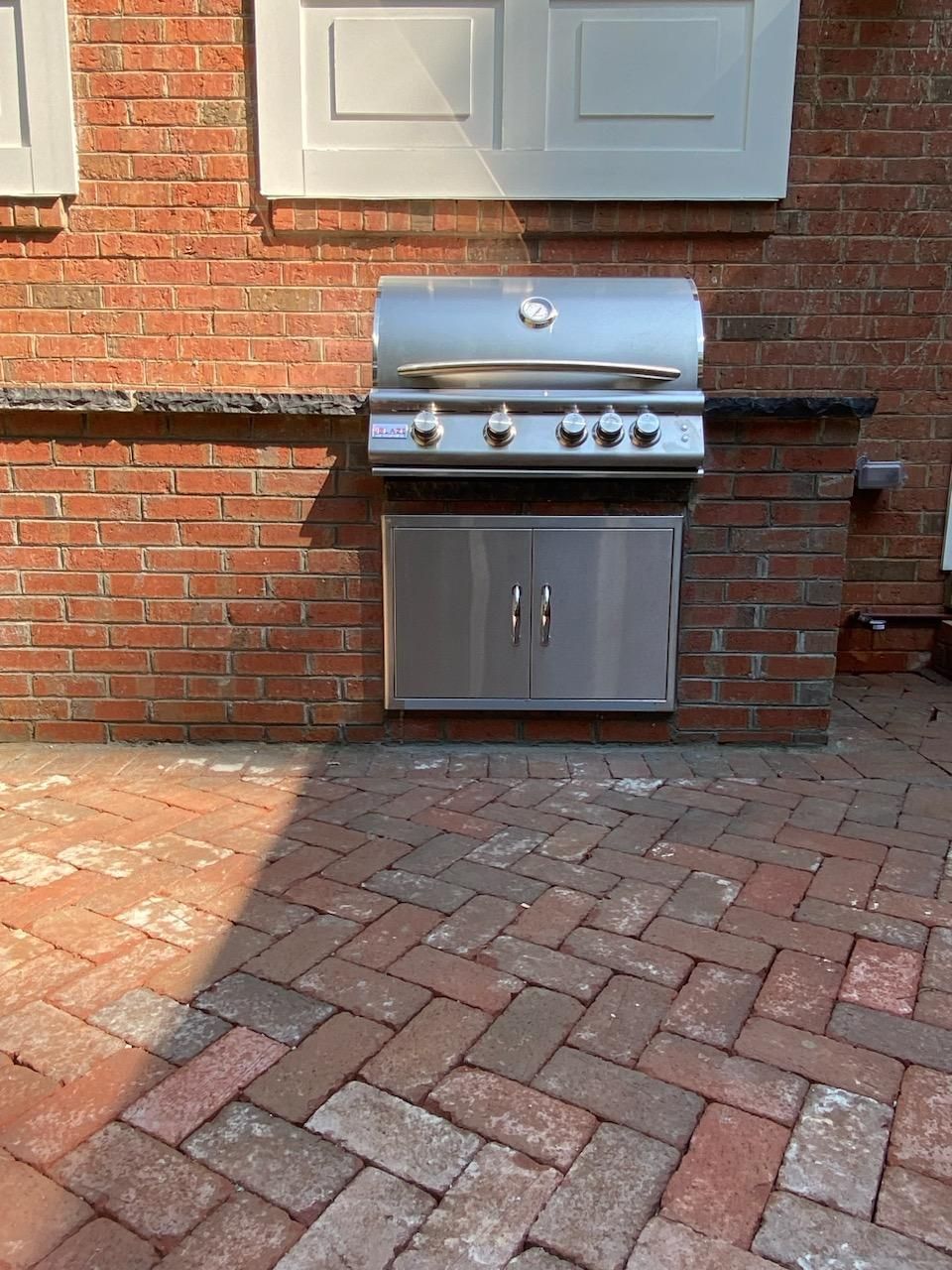 A stainless steel grill is mounted to a brick wall.