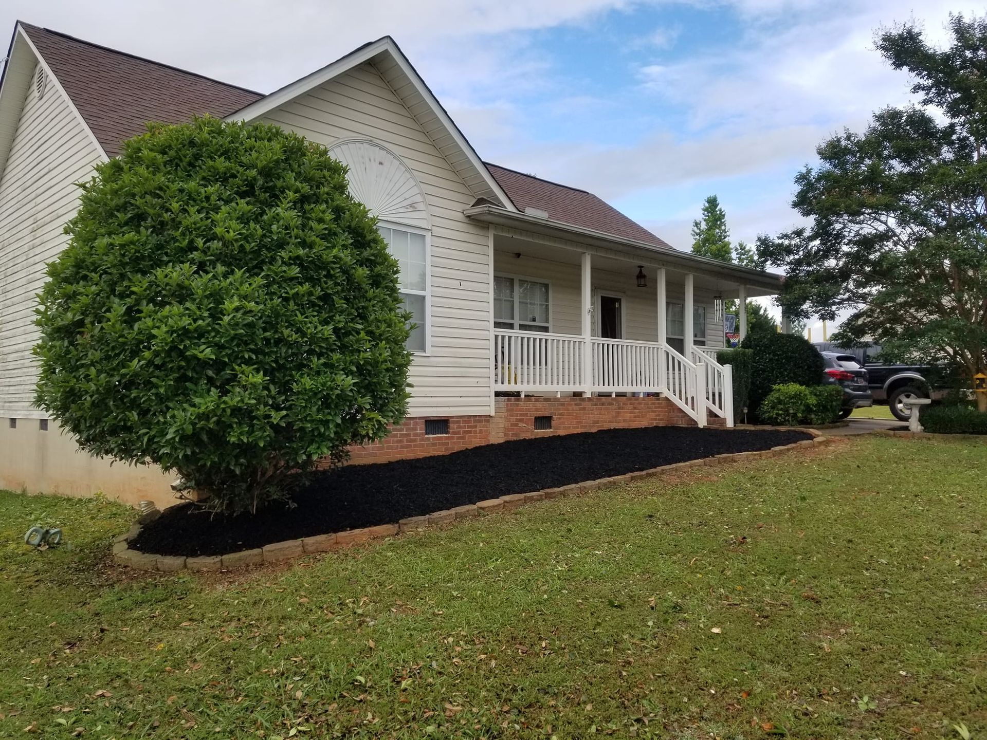 A white house with a porch and a tree in front of it. roebuck