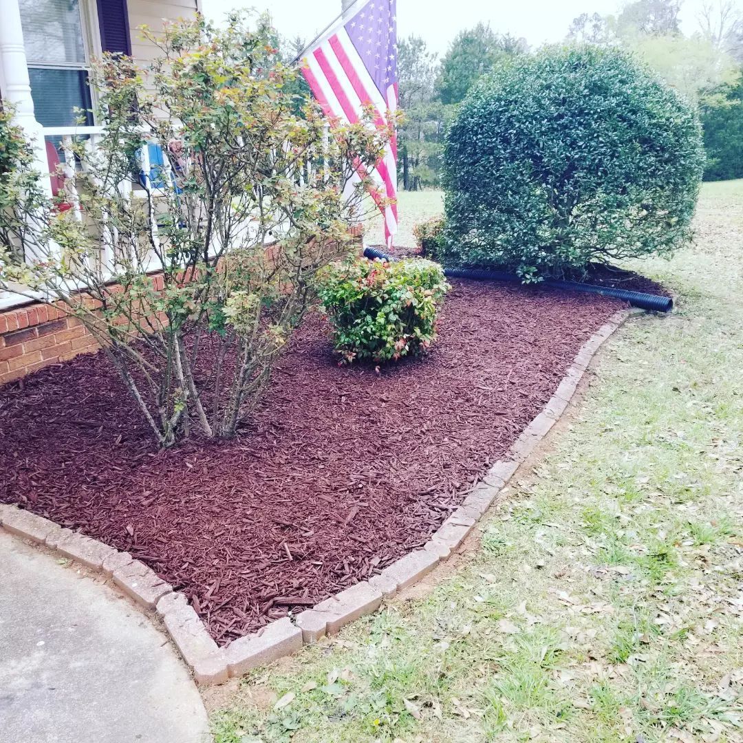 A garden with mulch and a flag in front of a house. lyman