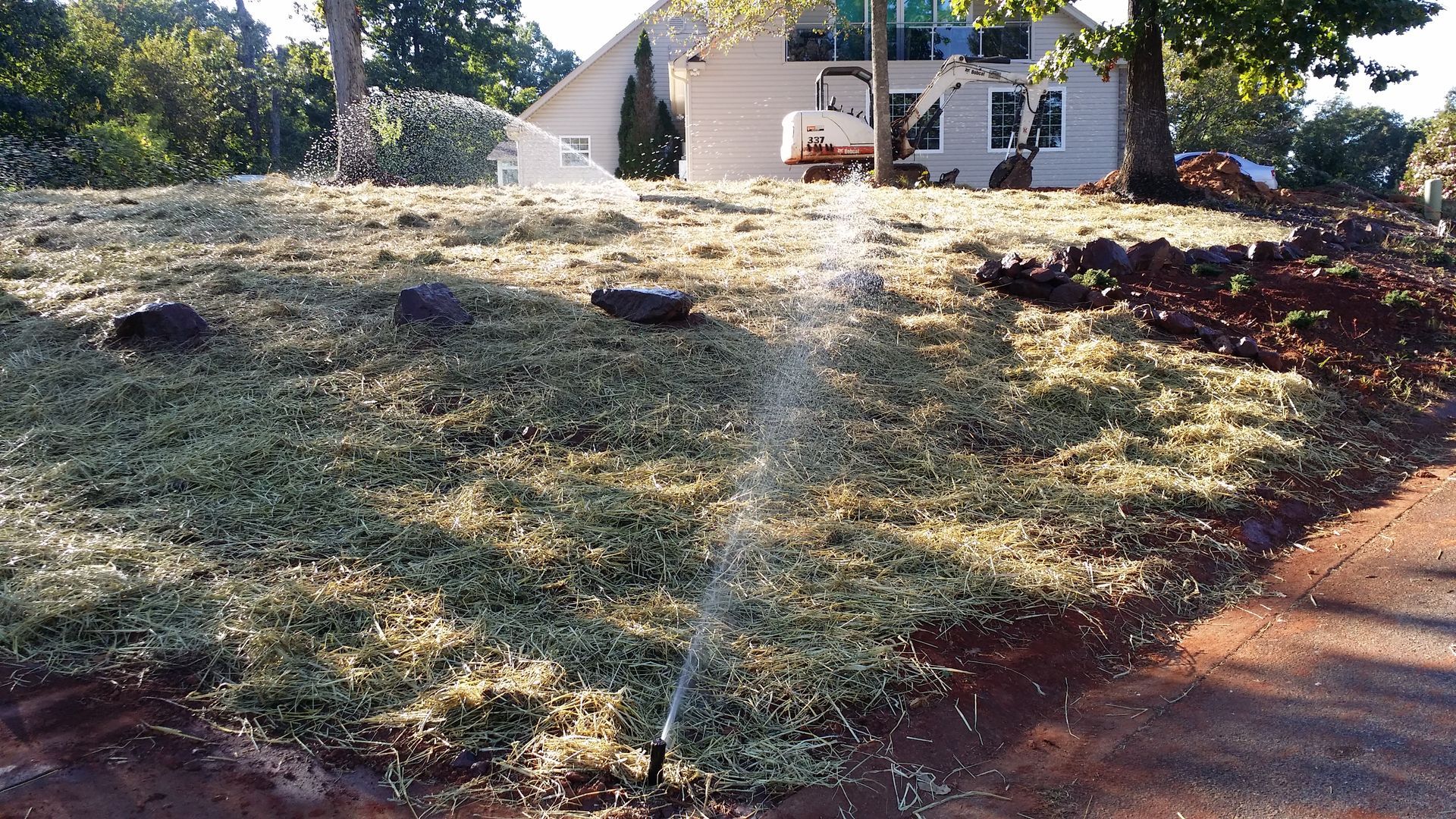 A sprinkler is spraying water on a grassy field in front of a house