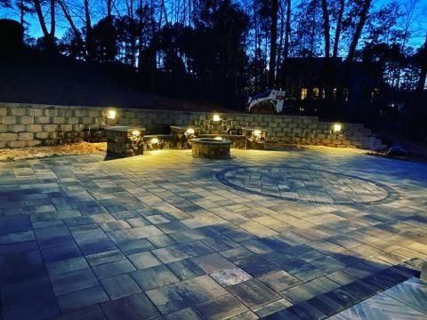 A patio with a fire pit and benches is lit up at night.