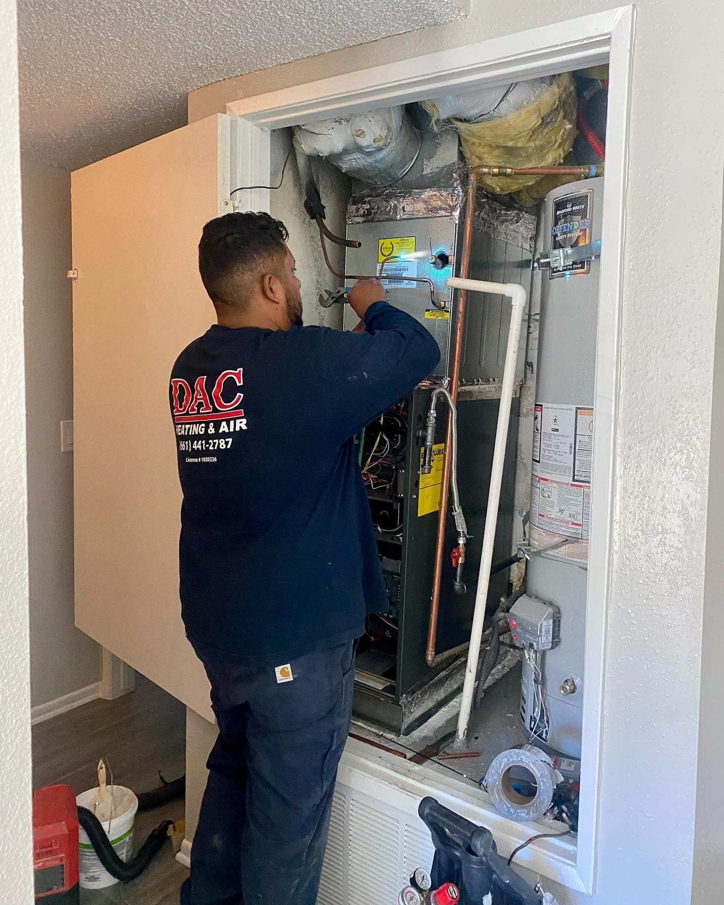 A man is working on an air conditioner in a closet.