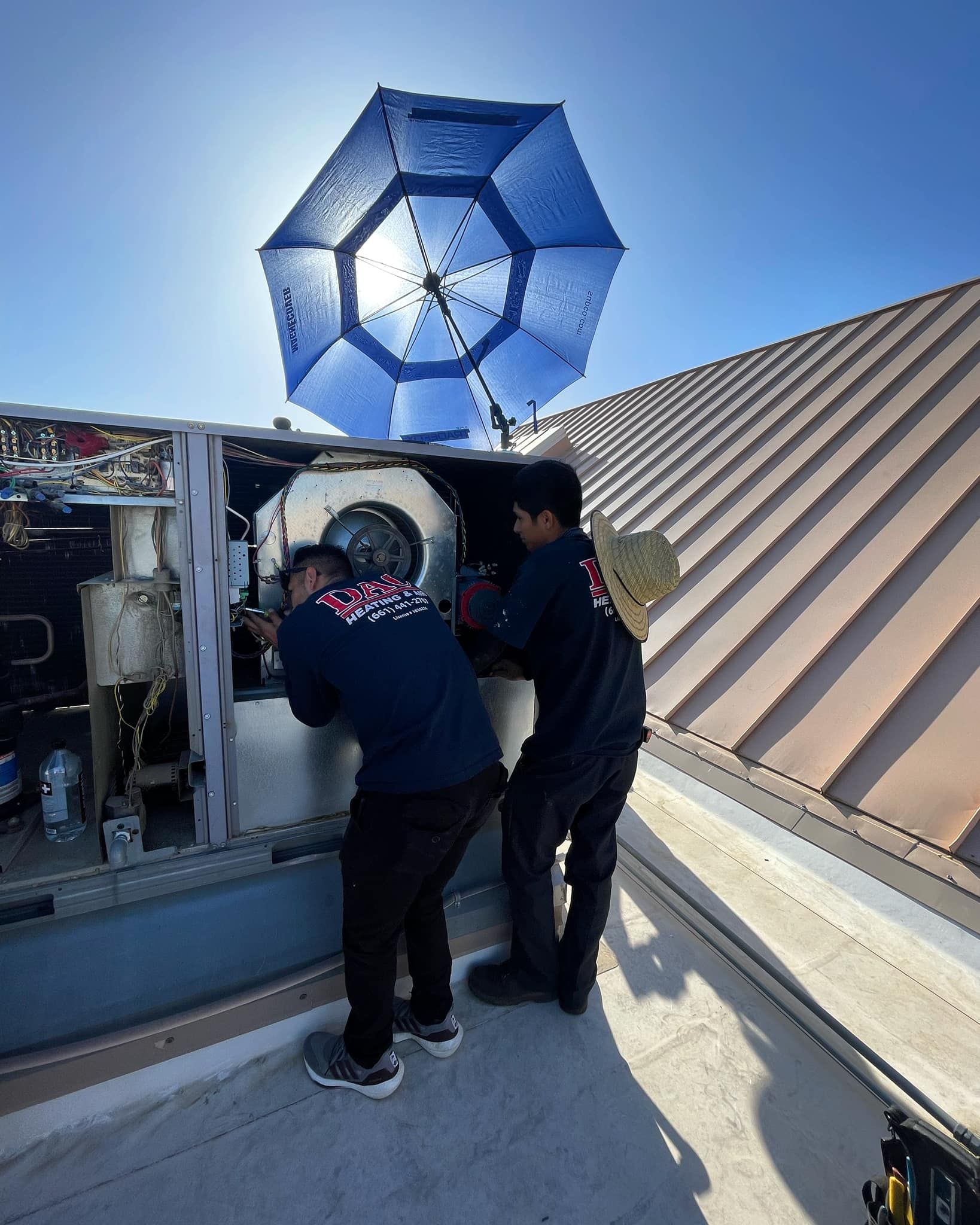 Two men are working on a machine on the roof of a building.