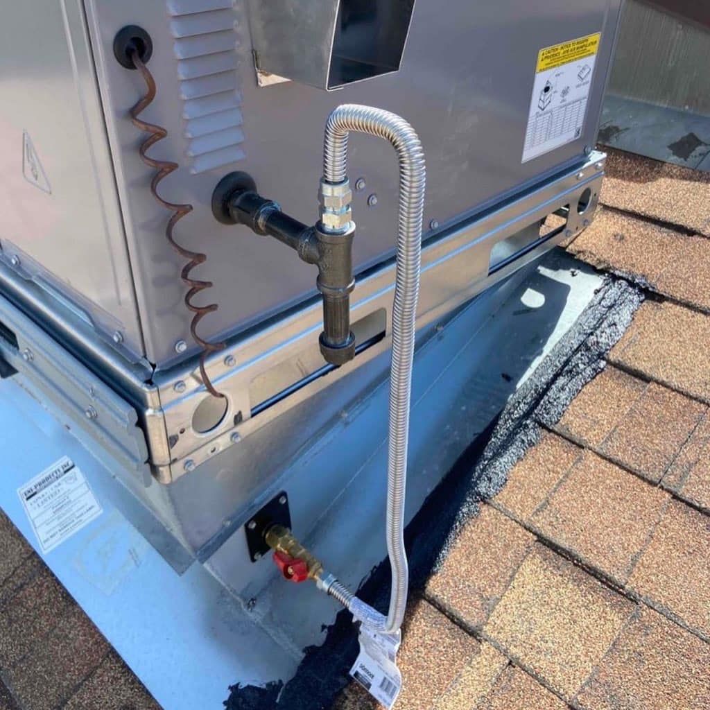 A close up of a hose attached to an air conditioner on a roof.