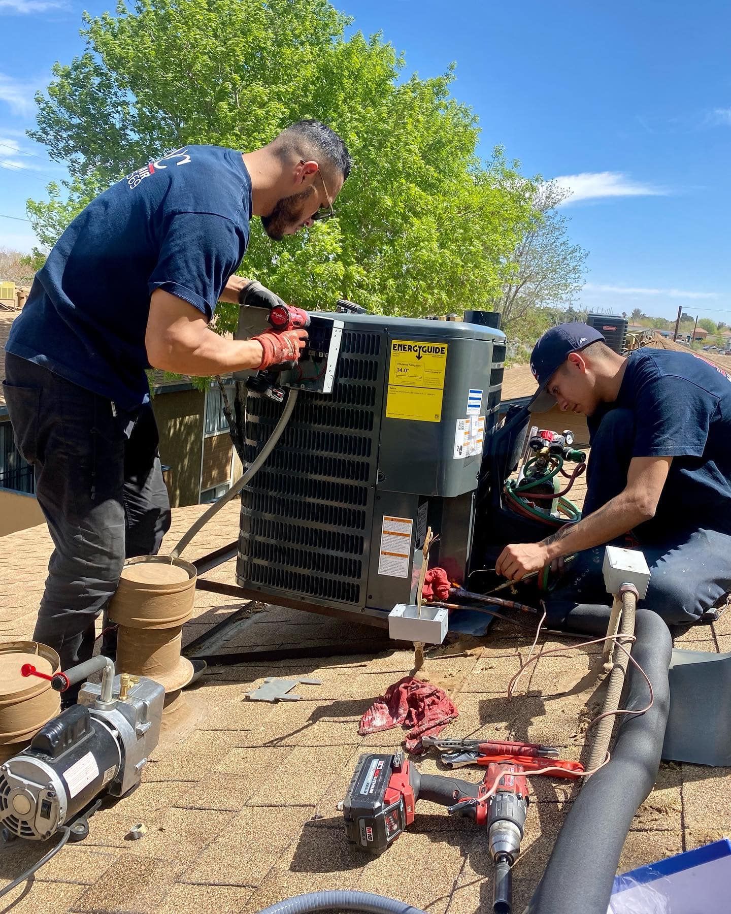 Two men are working on an air conditioner on a roof.