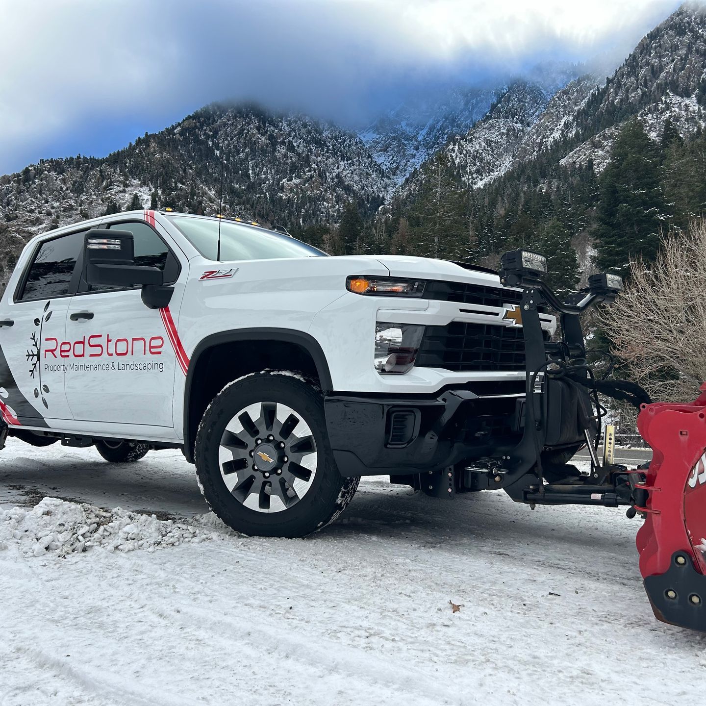 A white RedStone truck with a snow plow attached to it is parked in the snow.