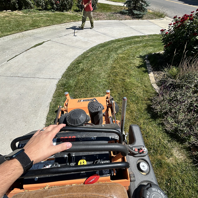 A person is riding a lawn mower down a sidewalk