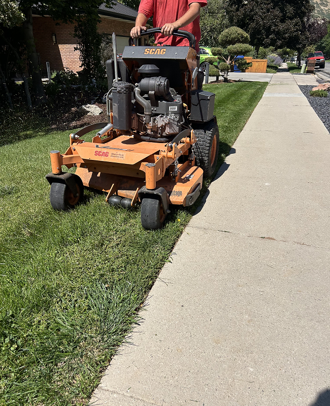 A man is riding a lawn mower down a sidewalk