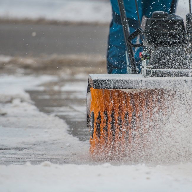 A person is using a snow blower to clear snow from the sidewalk.