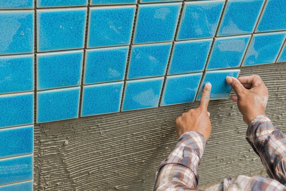 A Man Is Installing Blue Tiles On A Wall — Col Davies Pools In Port Stephens, NSW