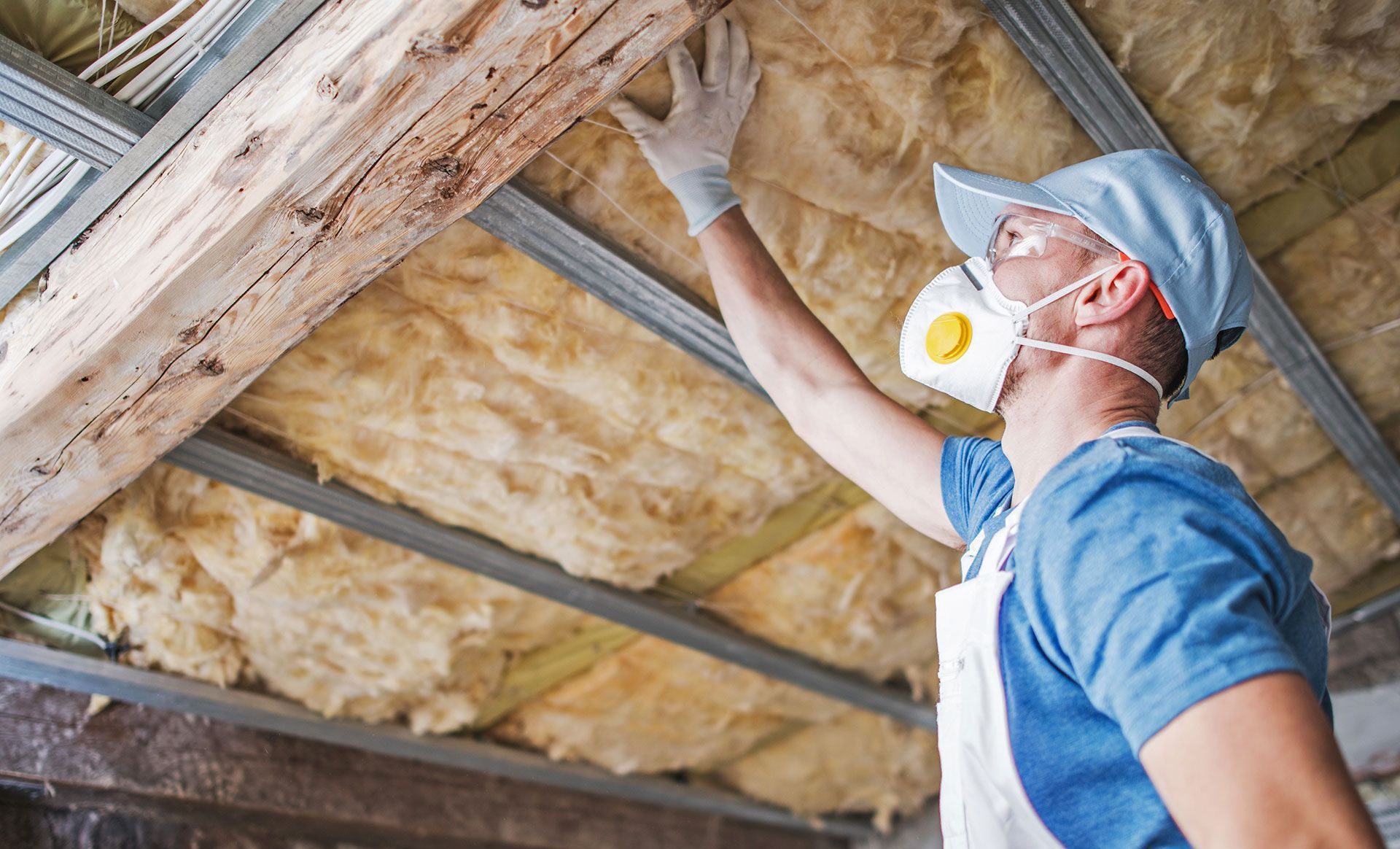 A man wearing a mask and gloves is insulating the ceiling of a house.