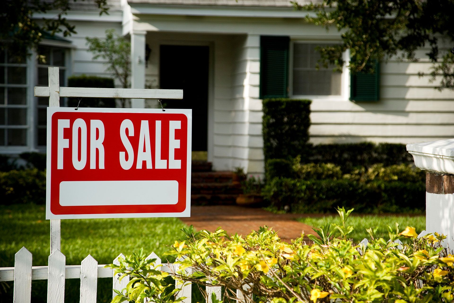 A for sale sign is in front of a white house.